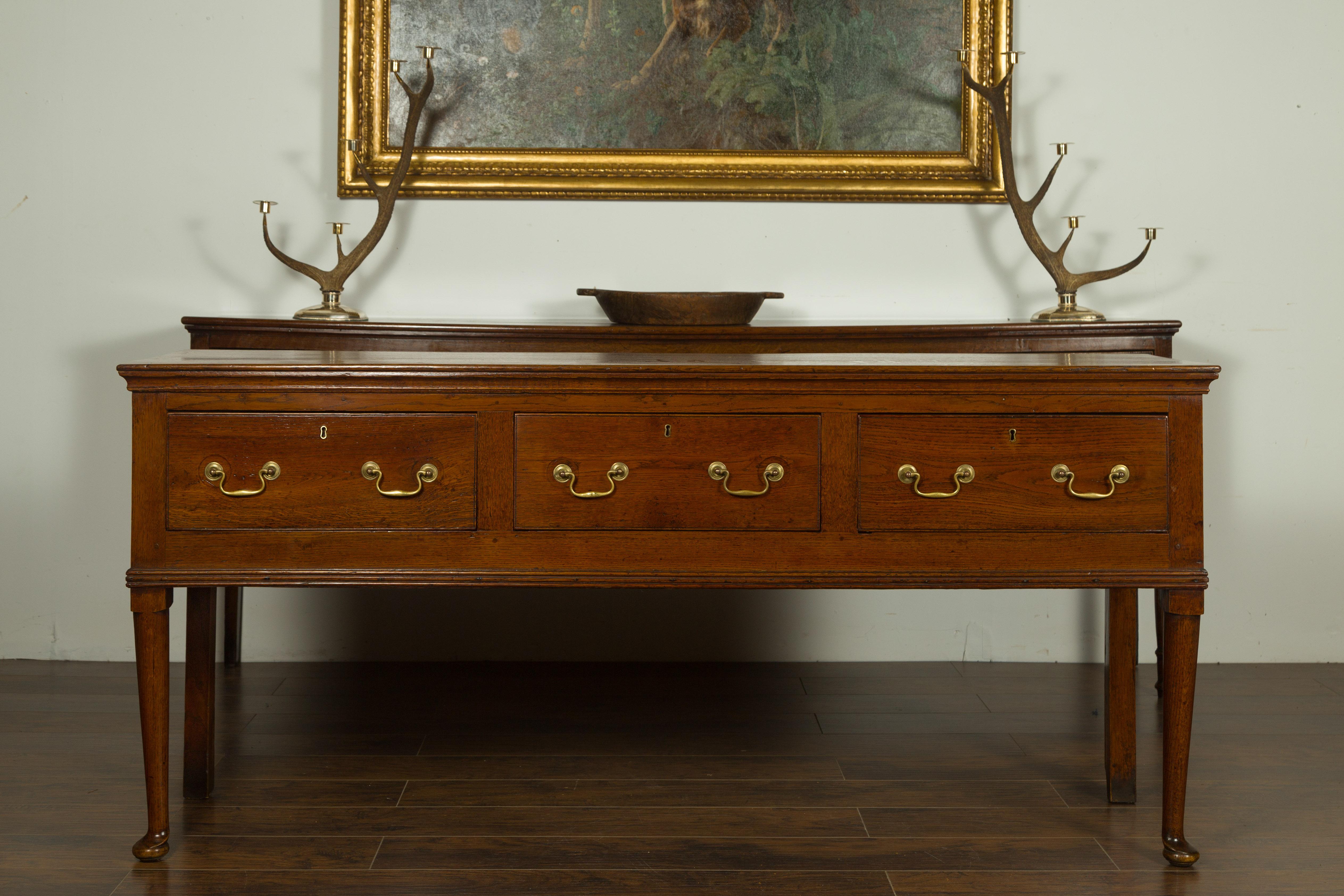An English Georgian period oak dresser base from the early 19th century, with three drawers and pad feet. Born in England during the first quarter of the 19th century, this oak dresser base features a rectangular top sitting above three dovetailed