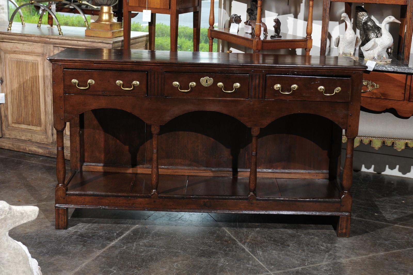 An English Georgian period walnut dresser base from the early 19th century, with three drawers, turned supports and pot board base. Born in England during the first quarter of the 19th century, this exquisite English walnut dresser base features a