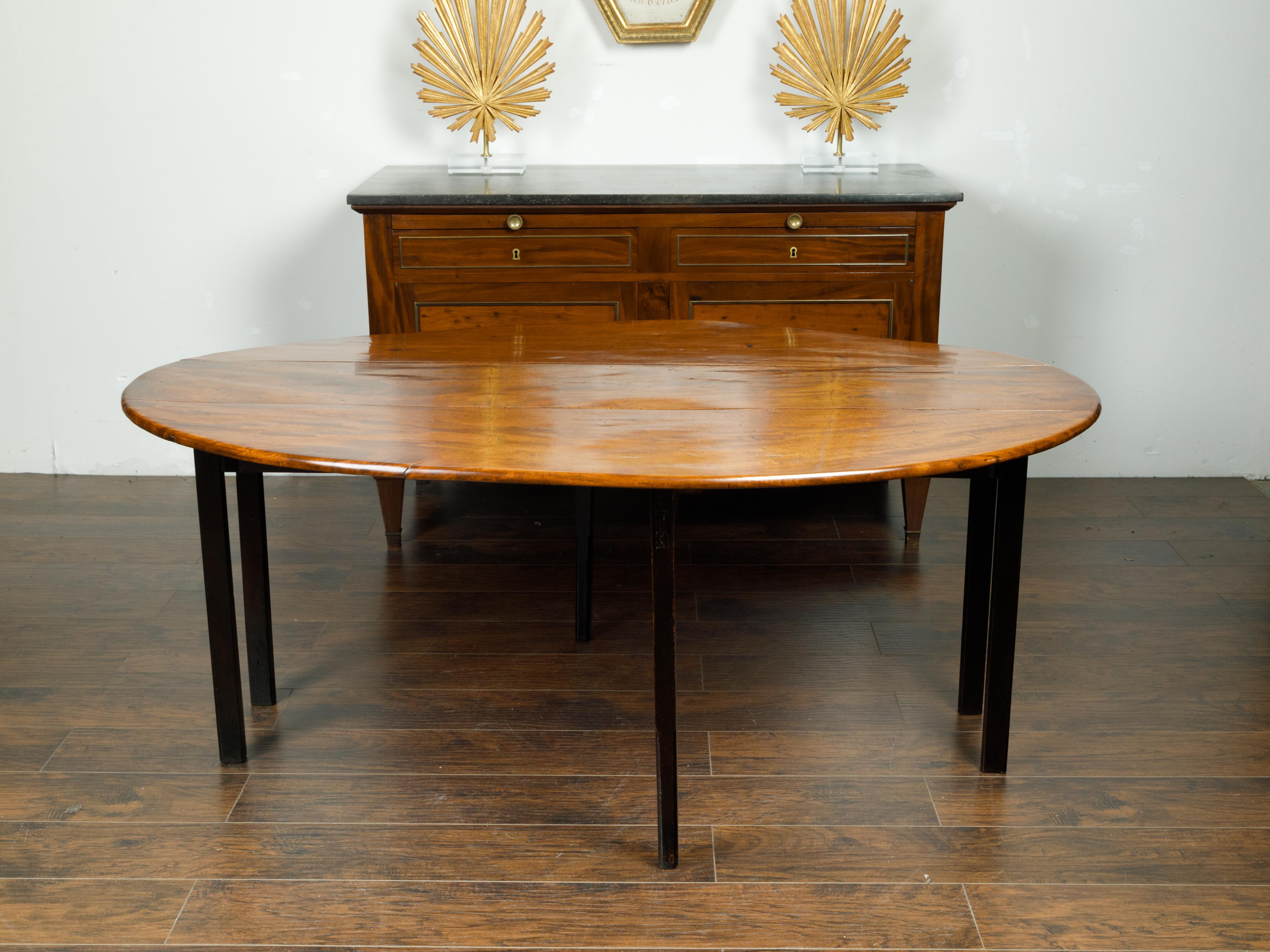 An English mahogany drop leaf dining table from the early 20th century, with oval top and ebonized legs. Created in England during the first quarter of the 19th century, this table features a mahogany veneered oval top with two drop leaves measuring