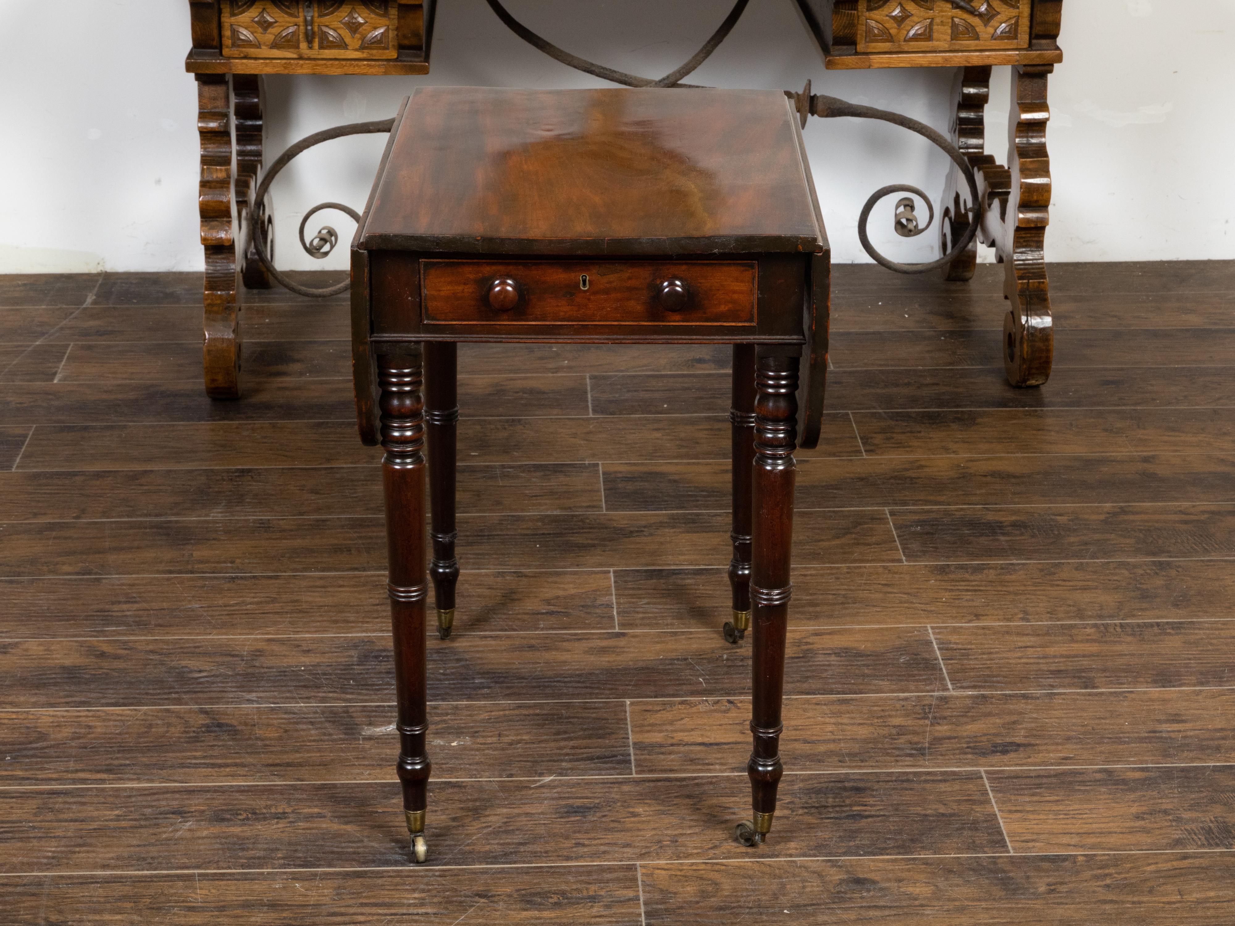 An English Regency period mahogany Pembroke table from the early 19th century, with two drop leaves, drawer, turned legs and brass casters. Created in England during the Regency period in the first quarter of the 19th century, this mahogany
