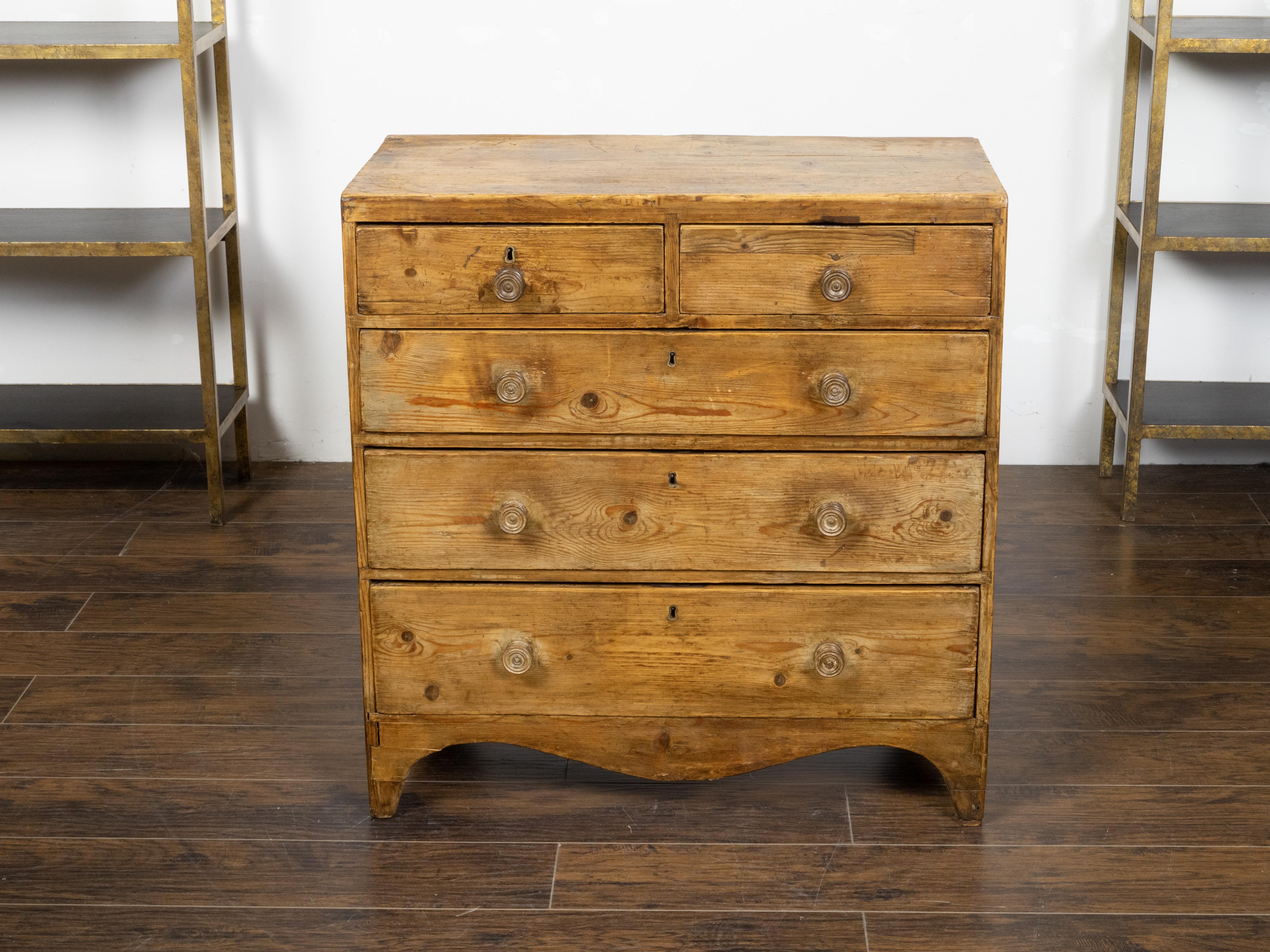 An English Regency period pine chest from the early 19th century, with five graduated drawers, turned wooden pulls, valanced skirt and distressed patina. Created in England during the Regency period in the early years of the 19th century, this pine