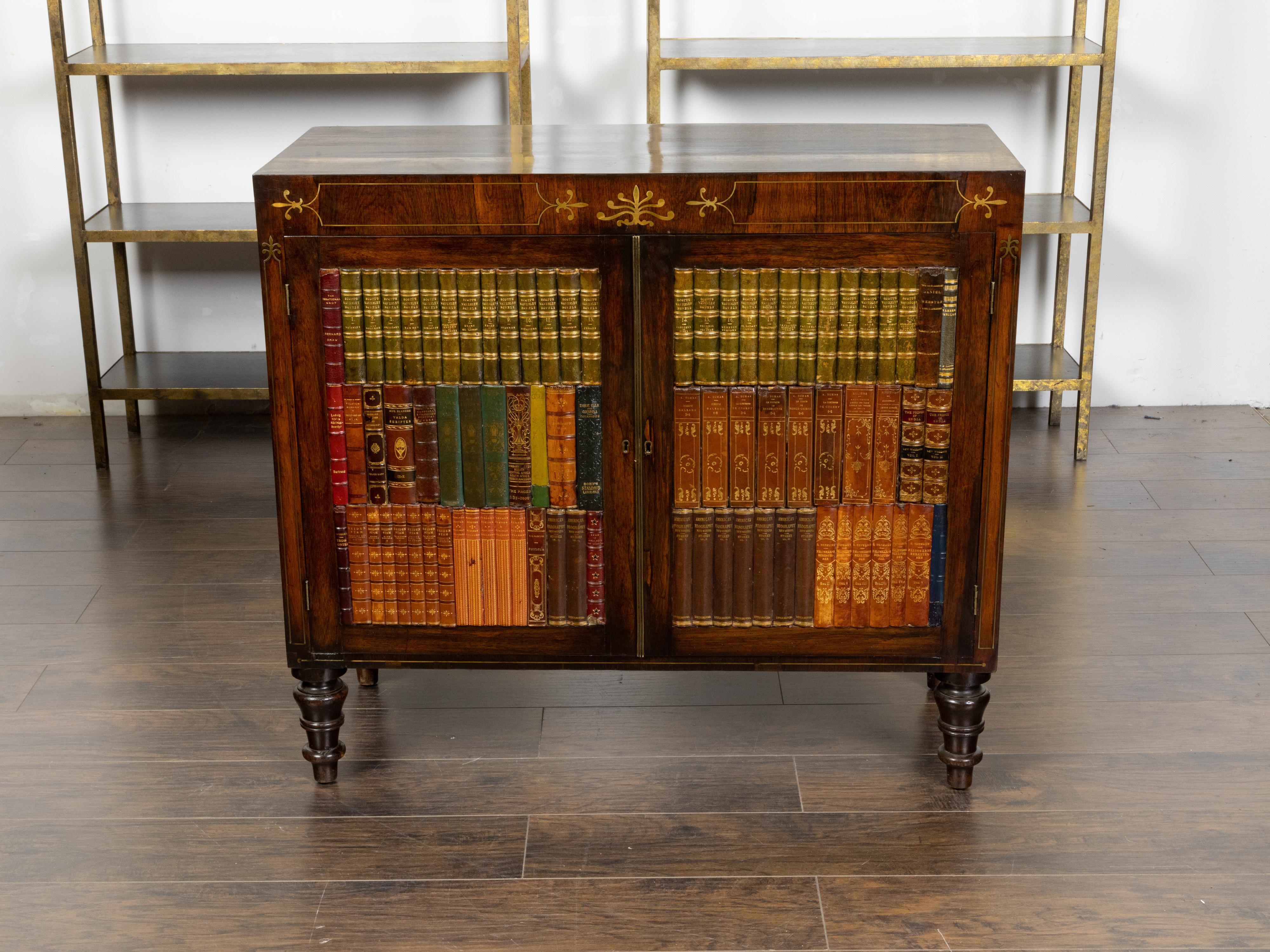 An English mahogany faux book cabinet from the mid 19th century, with foliage décor, brass inlay and turned feet. Created in England during the second quarter of the 19th century, this mahogany cabinet features a varnished rectangular top sitting