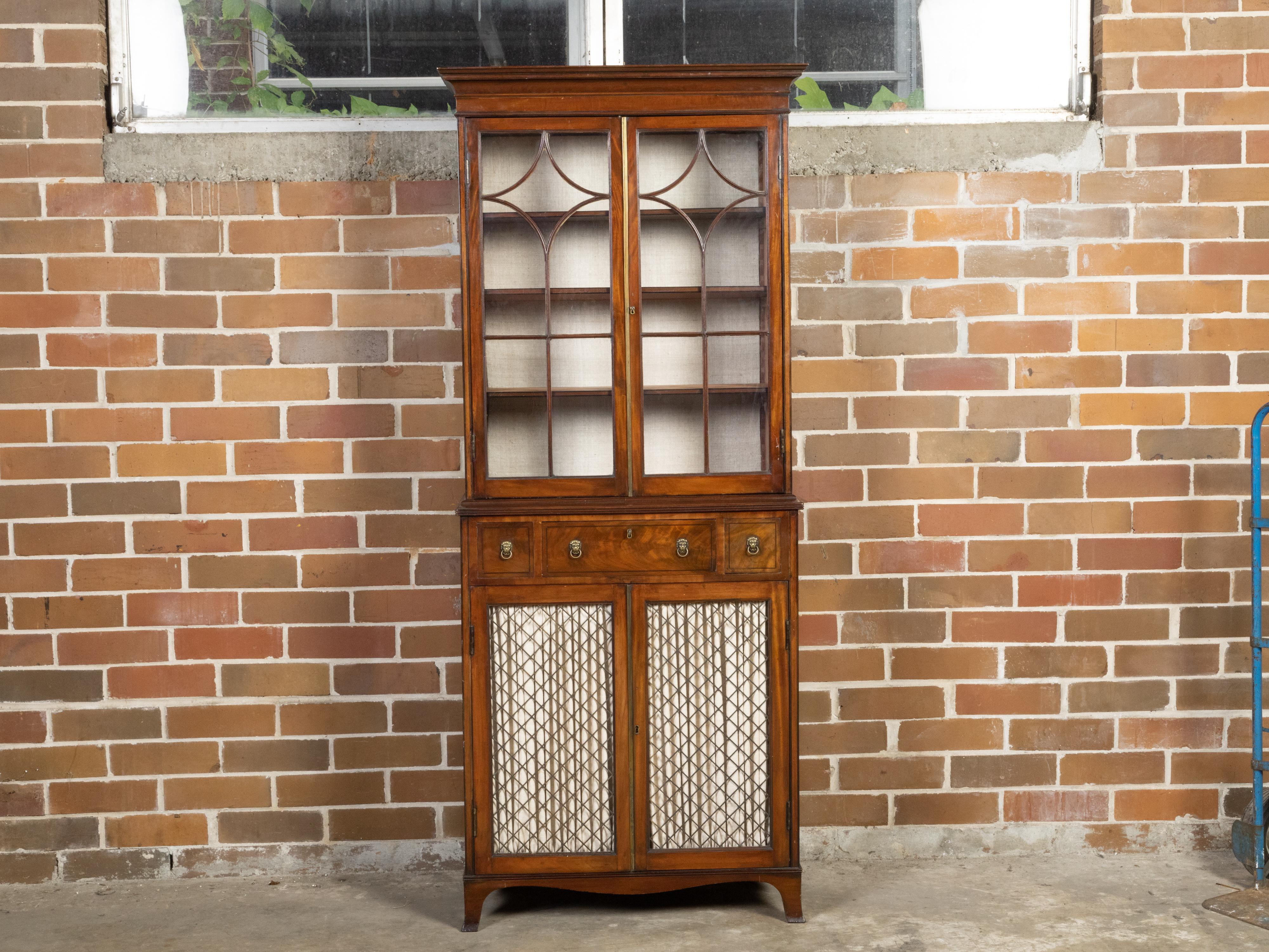 An English mahogany vitrine cabinet from the mid 19th century with glass doors, dark banding, fabric and drawers. Created in England during the second quarter of the 19th century, this vitrine cabinet features a slender silhouette perfectly