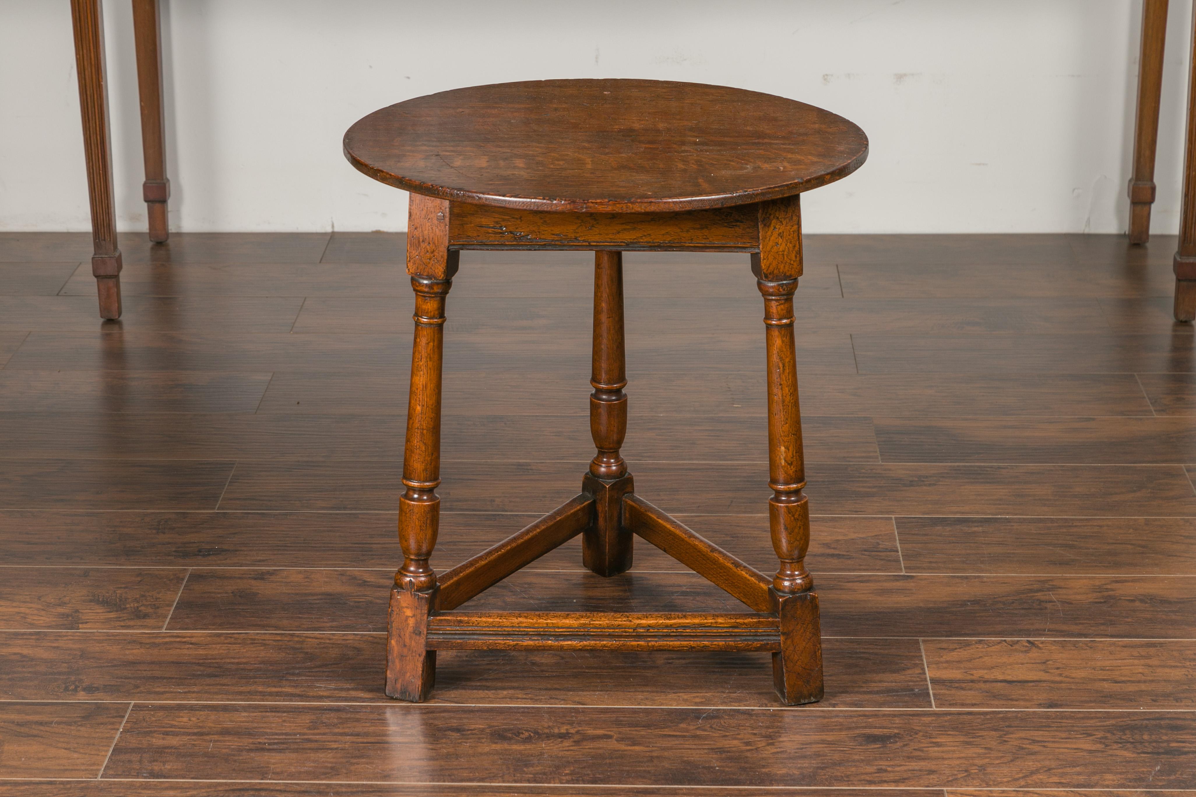 An English oak cricket table from the mid-19th century, with circular top, turned legs and stretchers. Born in England during the second quarter of the 19th century, this oak cricket table features a circular top sitting above a triangular apron,