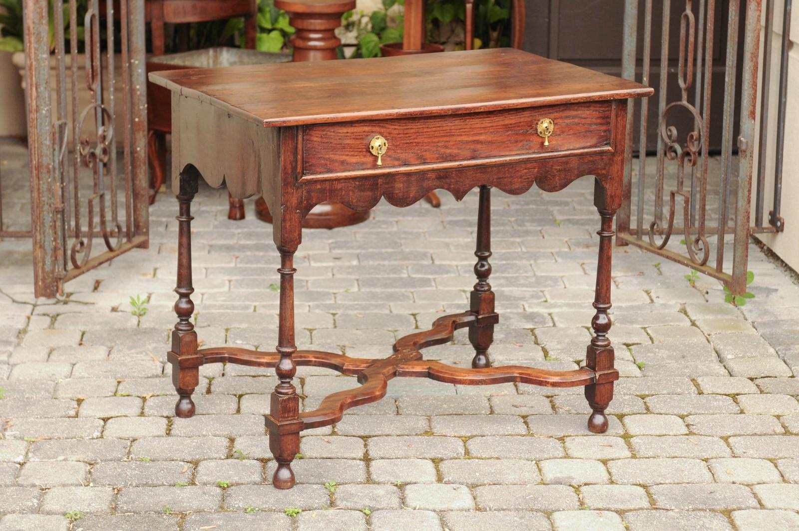 An English oak side table from the mid-19th century, with single drawer, turned legs and curving X-form cross-stretcher. Born in England during the second quarter of the 19th century, this exquisite side table features a rectangular top sitting