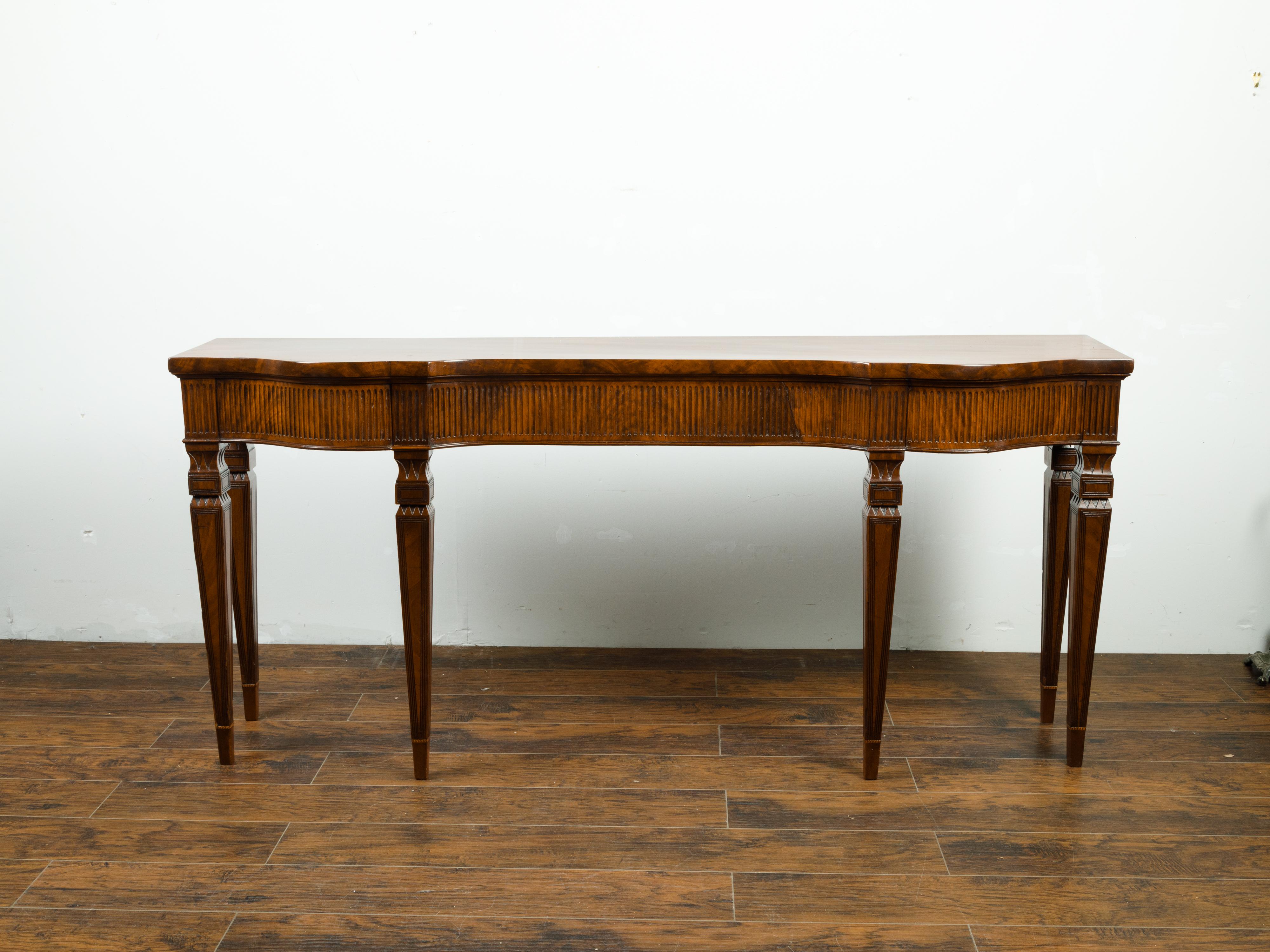 English mahogany console table from the mid 19th century, with fluted apron and tapered legs. Created in England during the 1850s, this mahogany console table features a shaped top sitting above a fluted serpentine apron. The ensemble is raised on
