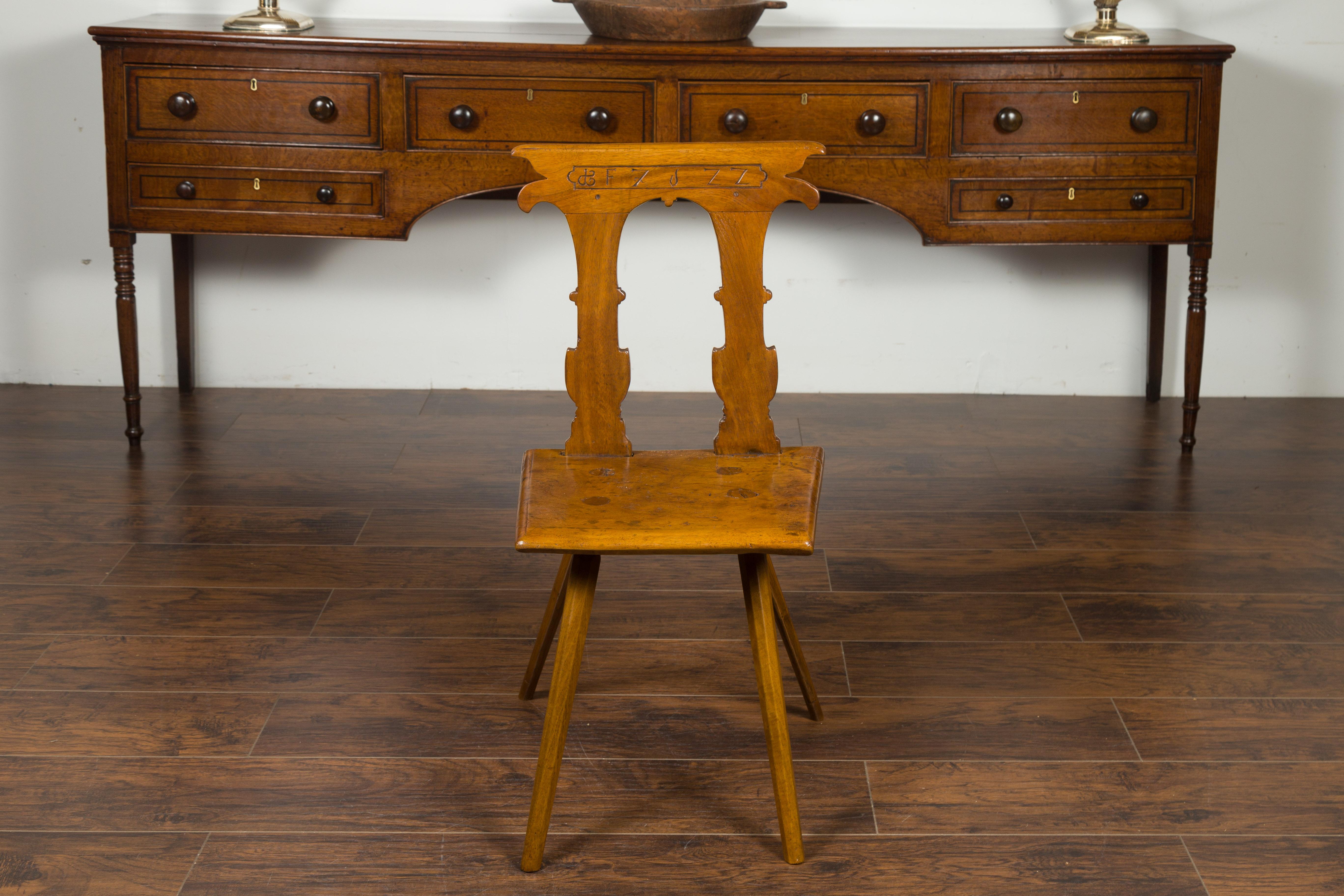 An English oak hall chair from the mid-19th century, with pierced back, carved letters and wooden seat. Created in England during the 1850s, this oak hall chair features a slightly slanted back, pierced in its center, carved on the sides and incised
