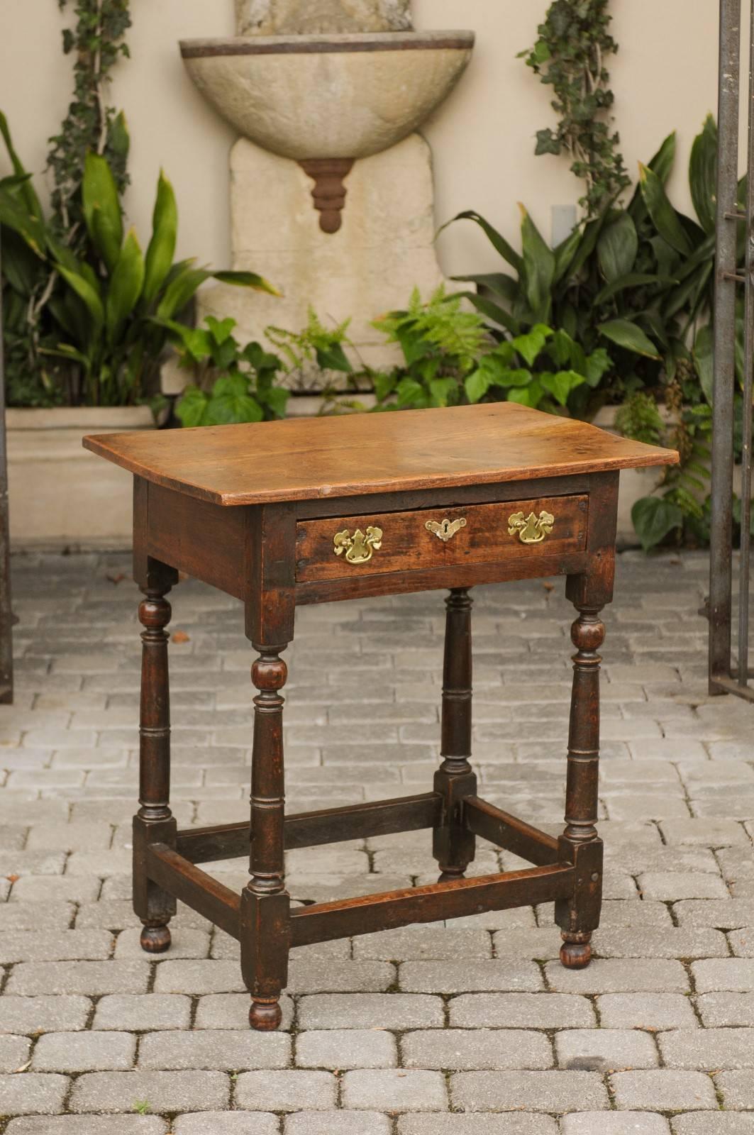 An English oak side table from the mid-19th century, with single drawer, turned legs and side stretcher. This English oak side table features a rectangular top sitting above a single drawer. This drawer is grooved for the runner and adorned with
