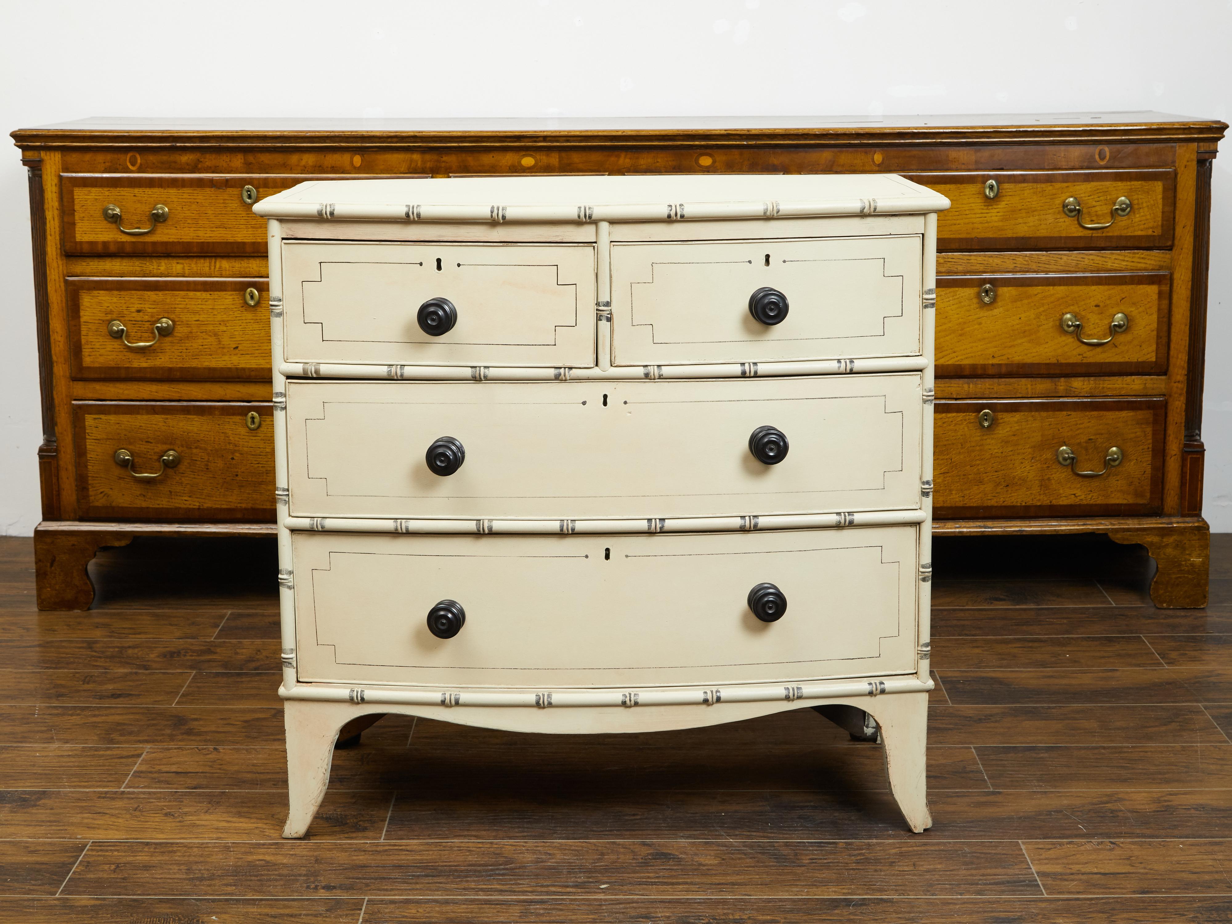 An English painted wood four-drawer bow front chest from the mid 19th century with faux bamboo accents and cartouche motifs. Created in England during the 1850s, this chest features a rectangular top with curving front, sitting above four drawers
