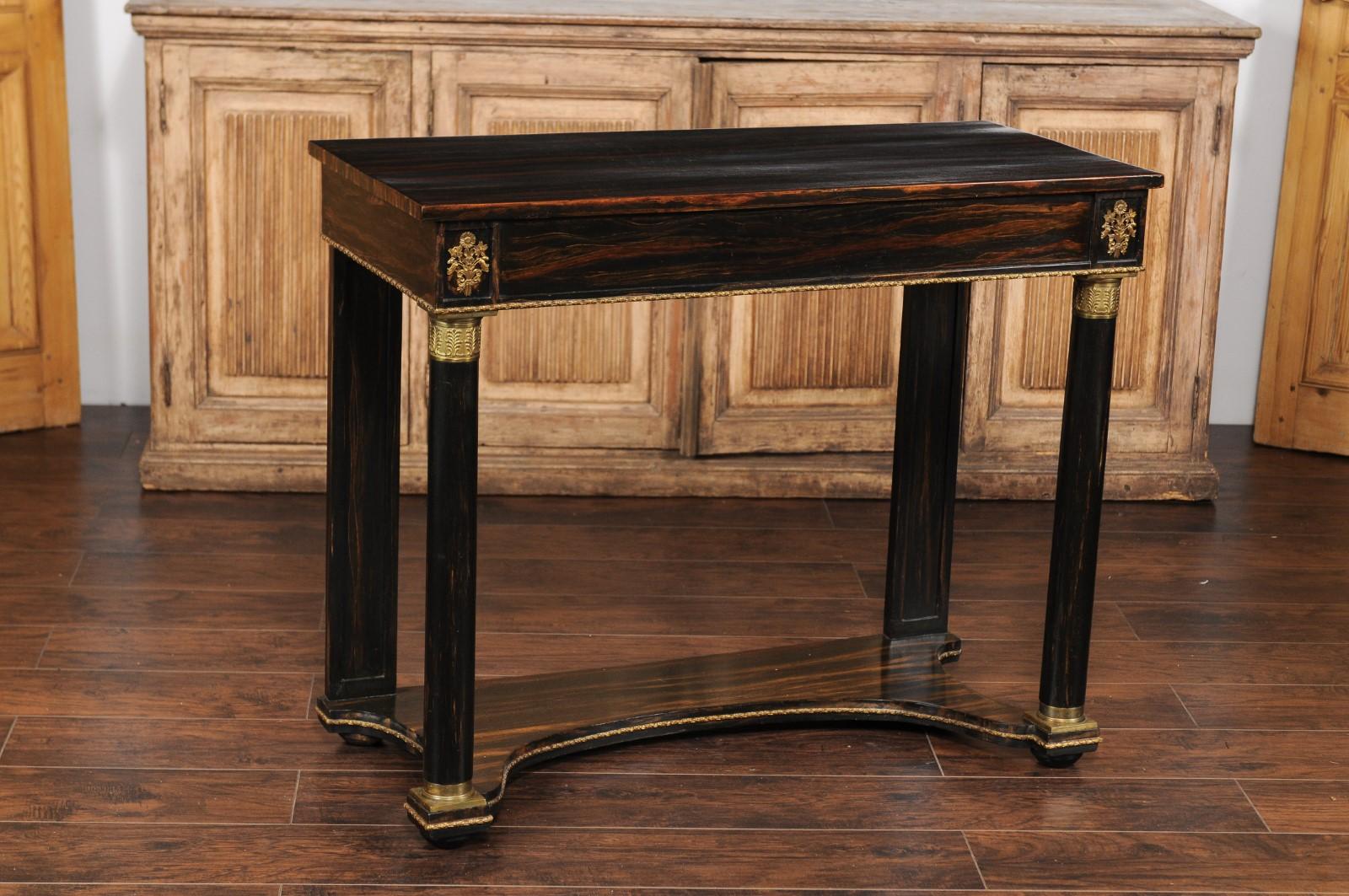 An English Regency style faux-painted rosewood console table from the mid-19th century, with bronze mounts and lower shelf. Born in England during the 1850s, this elegant console table features a rectangular top sitting above a lovely apron, adorned