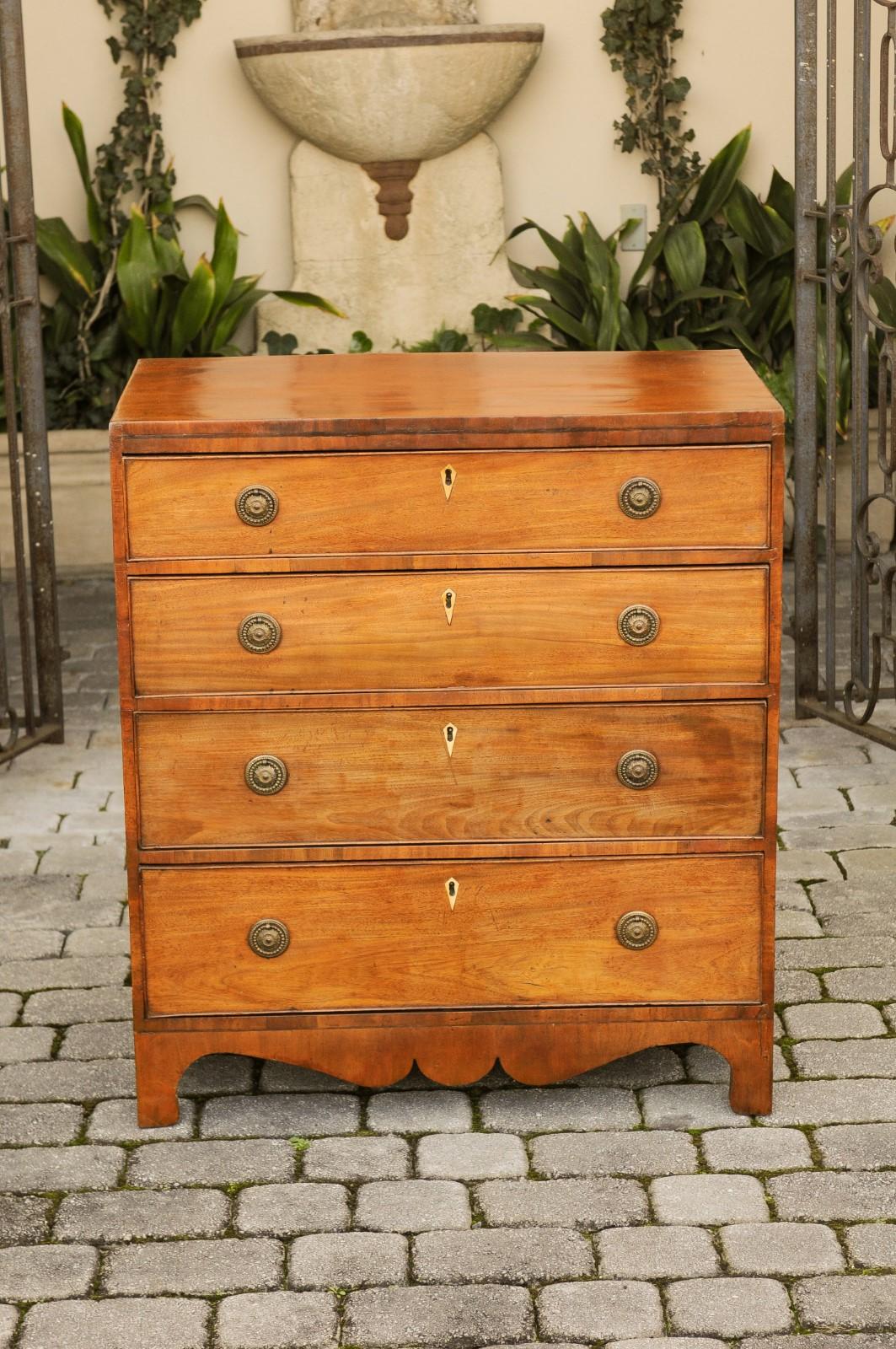 An English mahogany four-drawer commode from the mid-19th century, with graduated drawers and scalloped skirt. This English mahogany chest features a rectangular top sitting above four graduated drawers, each fitted with brass hardware and an inlaid
