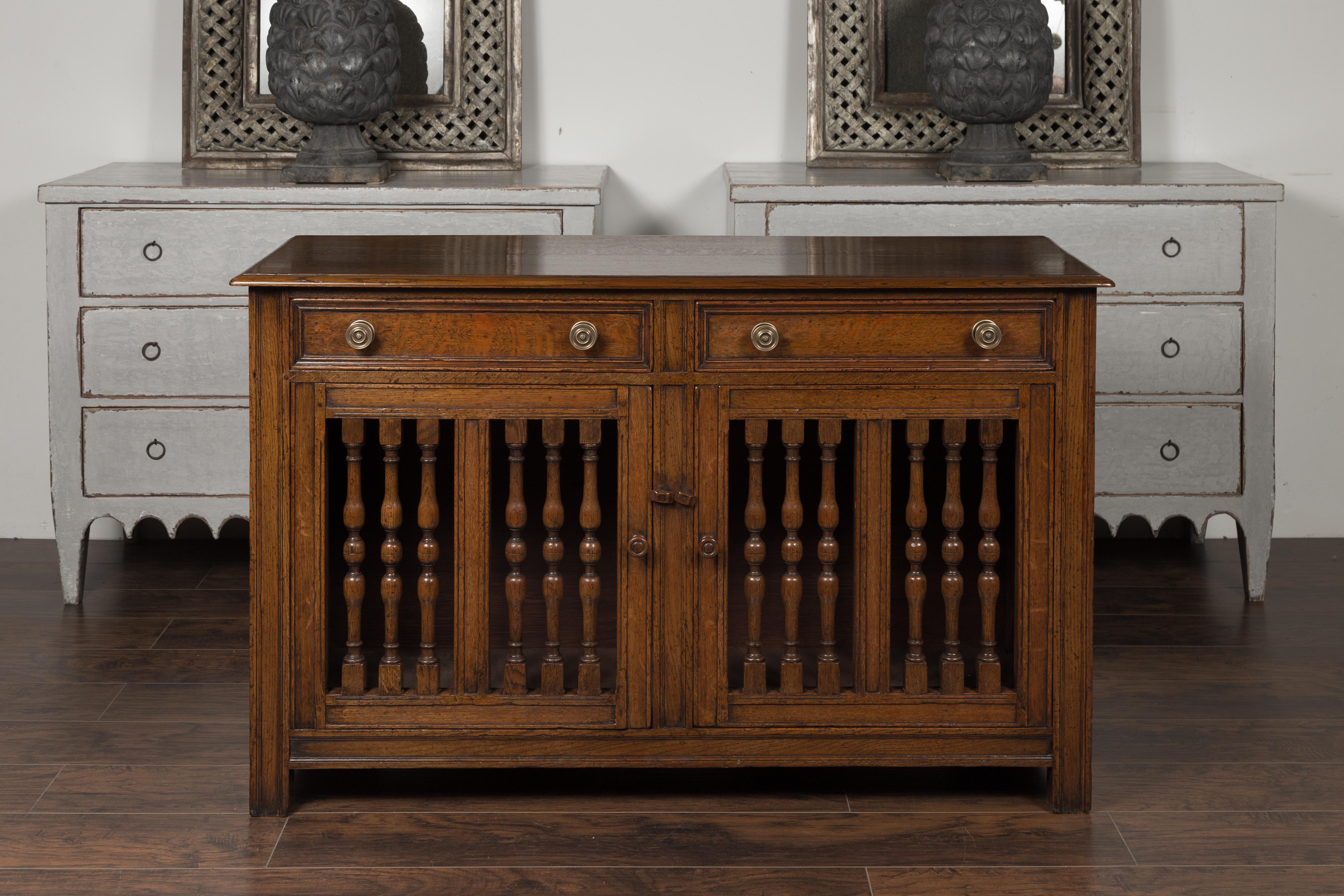 An English oak buffet from the mid-19th century, with two drawers, two doors and turned balusters. Born in England during the third quarter of the 19th century, this oak buffet features a rectangular top with beveled edges, sitting above two