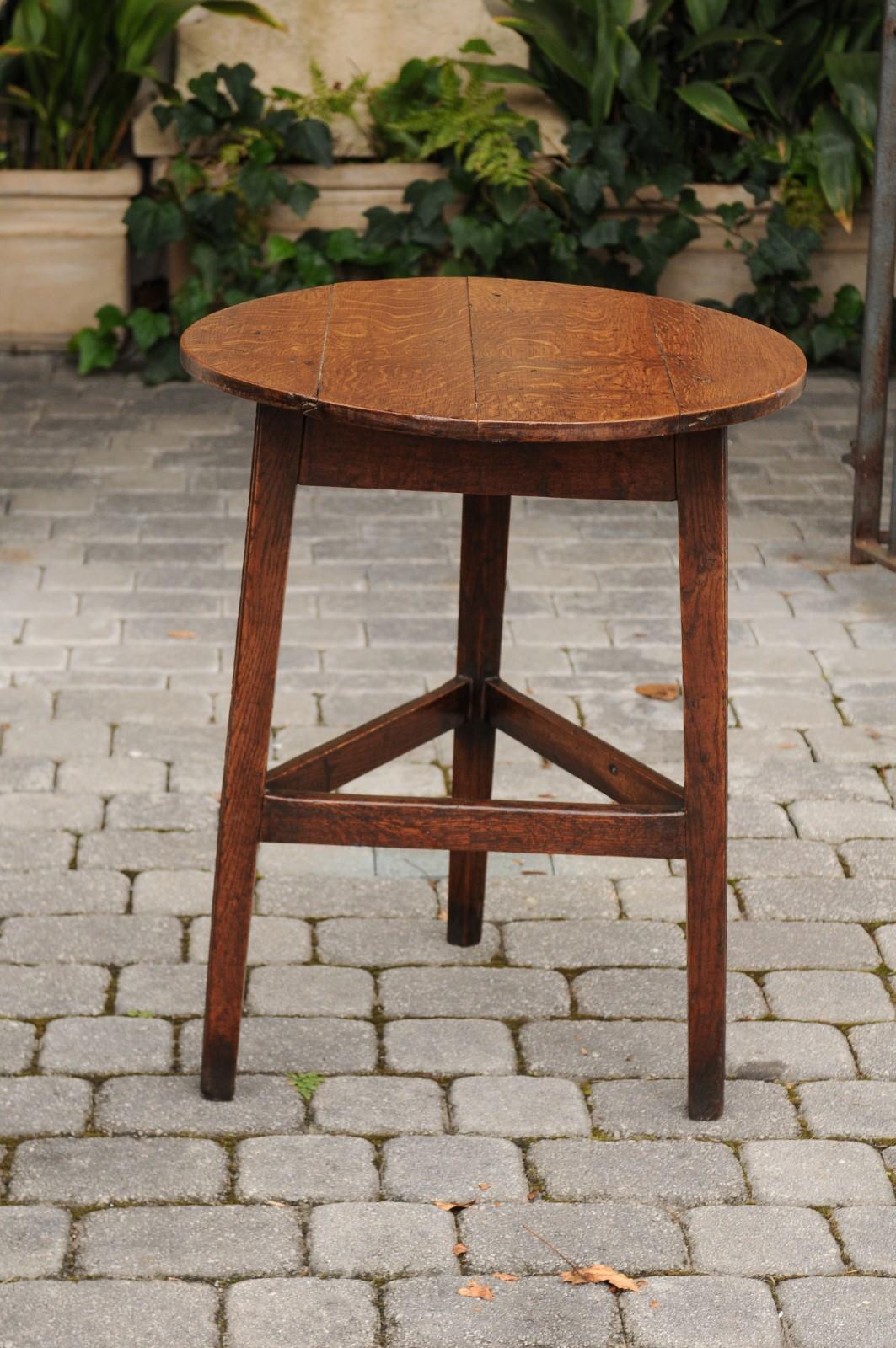 An English oak cricket table from the mid-19th century, with circular top and triangular side stretcher. Born during the third quarter of the 19th century, this rustic cricket side table features a circular top, sitting above a simple triangular