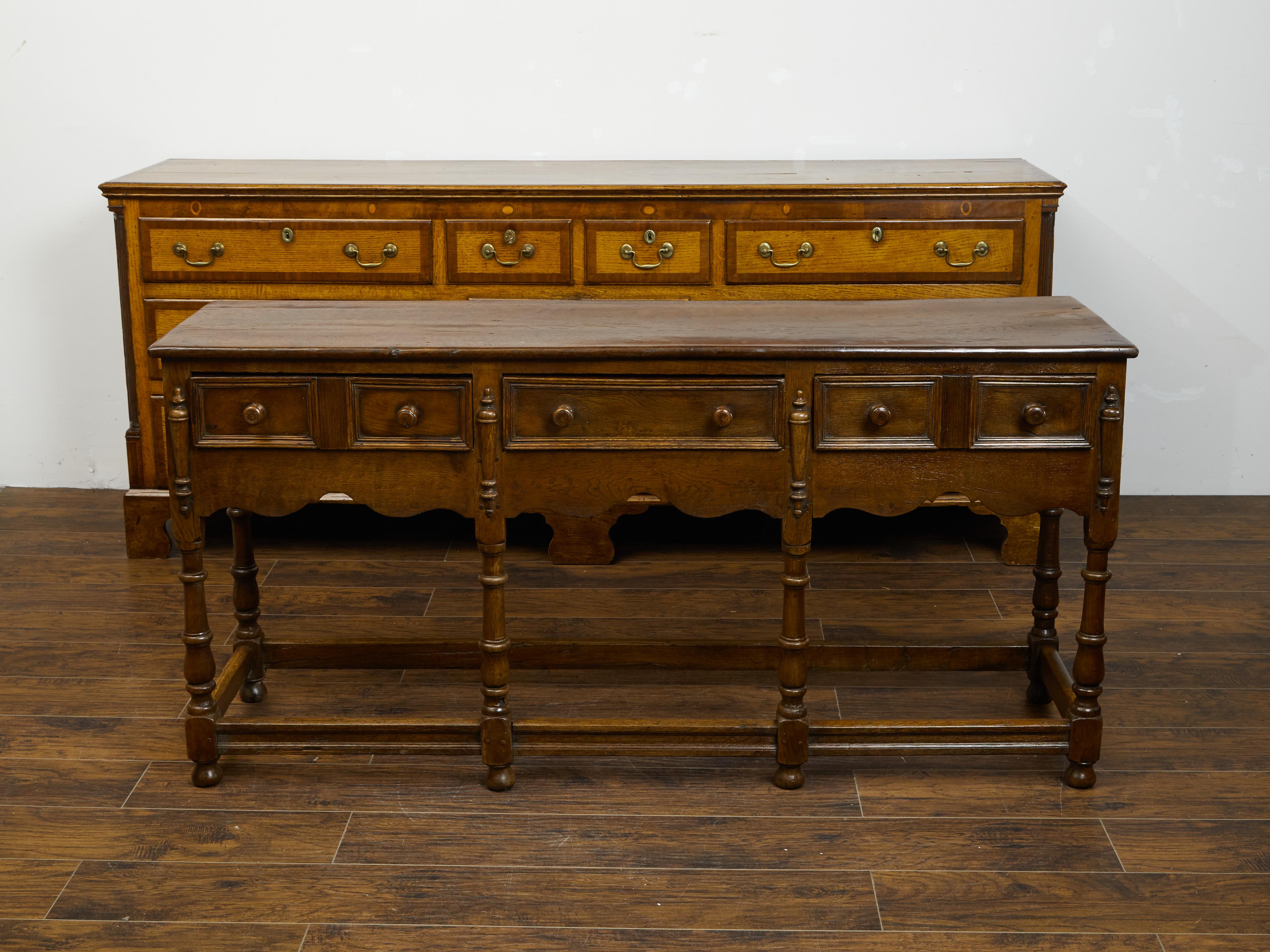 An English oak dresser base from the mid 19th century, with three drawers, scalloped apron and turned legs. Created in England during the third quarter of the 19th century, this oak dresser base features a rectangular top sitting above three drawers