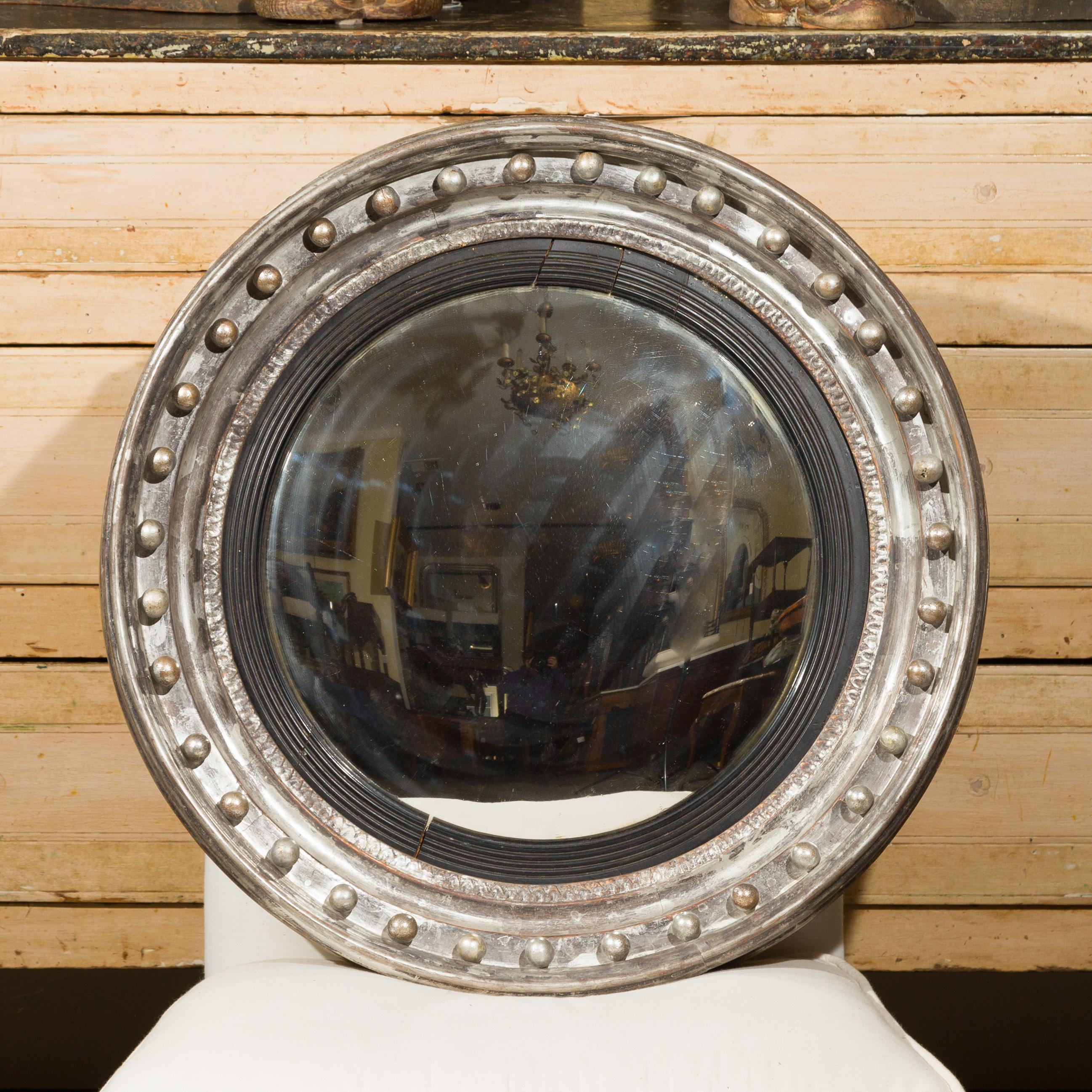 An English silver leaf bull's-eye convex girandole mirror from the mid-19th century with ebonized reeded accents. Born in England during the third quarter of the 19th century, this circular mirror features a convex mirror plate, surrounded by a