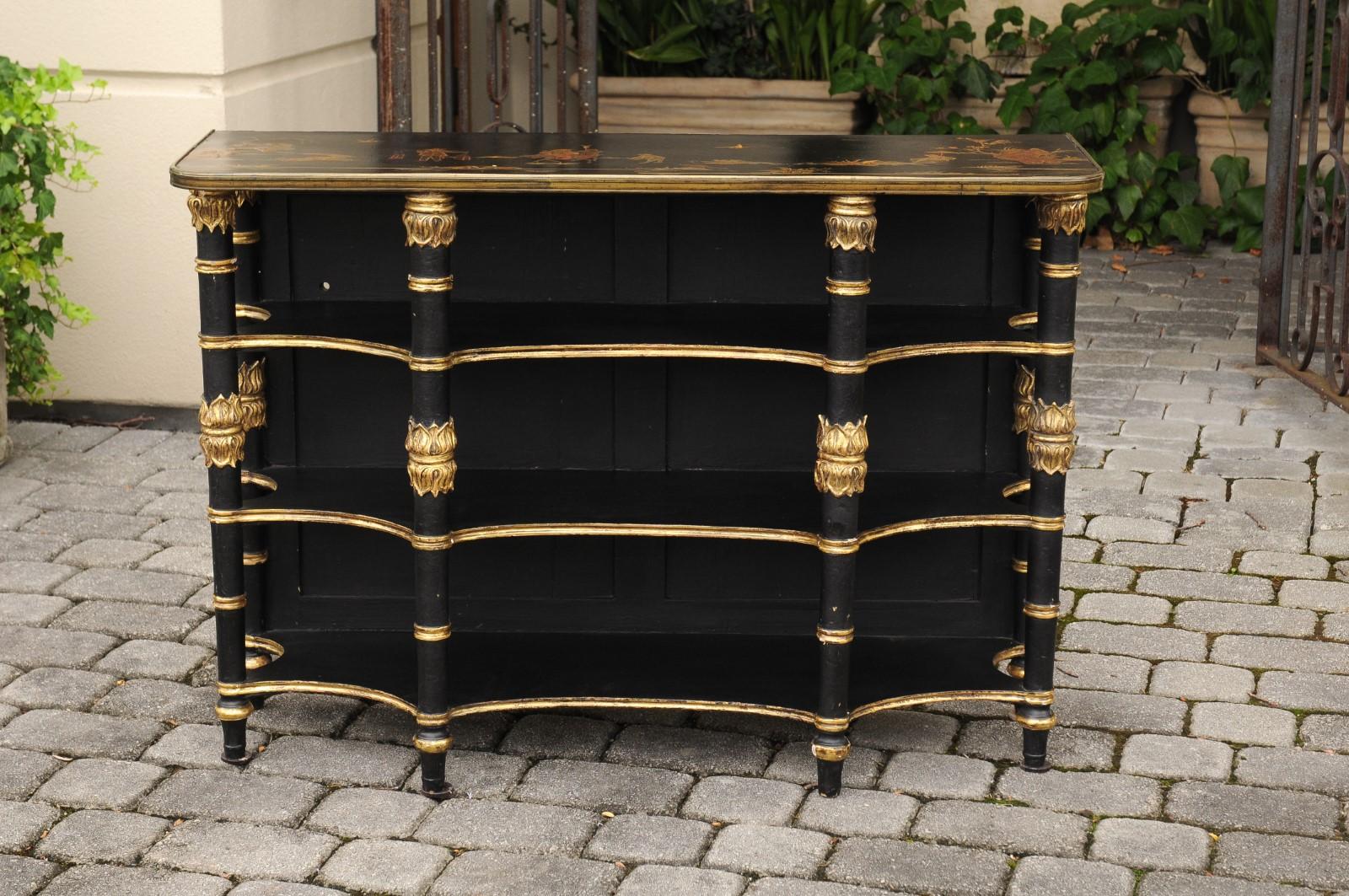 An English ebonized three-tiered freestanding shelf from the turn of the century, with chinoiserie decor and gilded accents. Born in England around 1900, this exquisite ebonized three-tiered freestanding shelf captivates with its chinoiserie