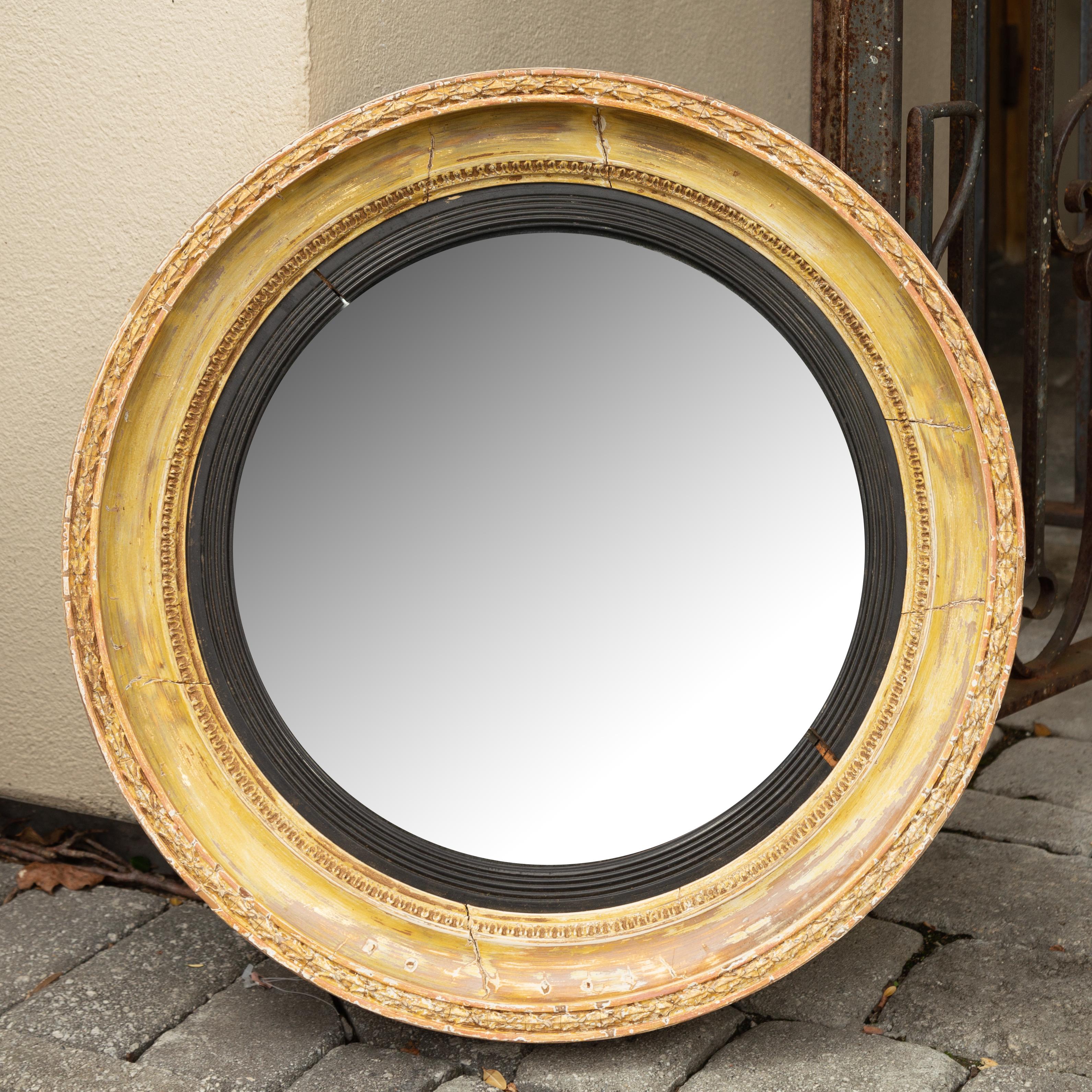 An English painted bullseye convex mirror from the late 19th century with ebonized reeded accents, distressed finish and foliage motifs. Born in England during the third quarter of the 19th century, this handsome piece features a convex mirror
