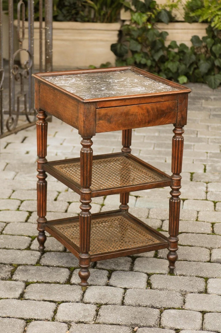 An English mahogany étagère from the late 19th century, with cane shelves, single drawer and marble top. Born in England during the third quarter of the 19th century, this elegant étagère features a square-shaped grey variegated marble top with