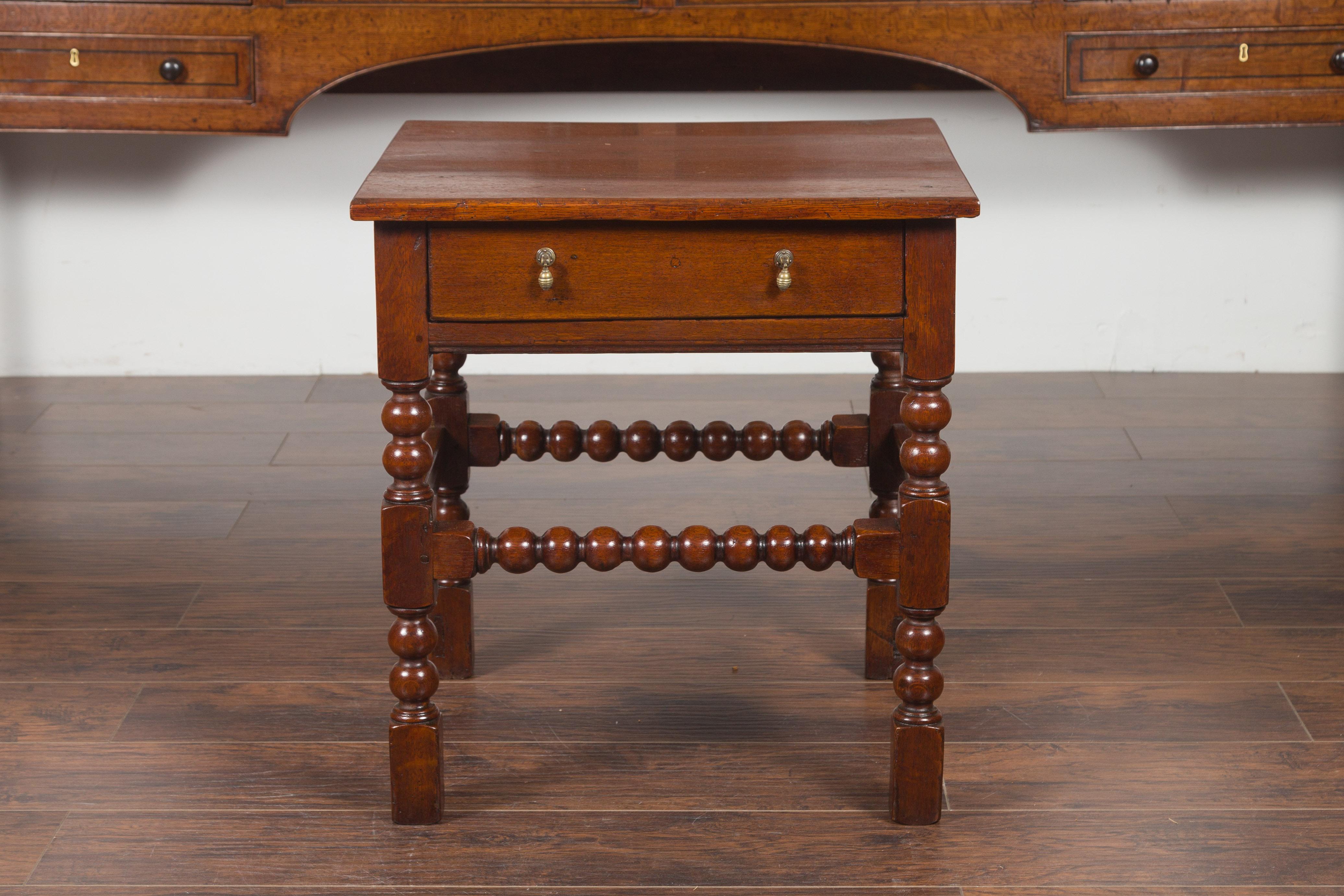 An English oak bobbin legs side table from the late 19th century, with single drawer and stretchers. Created in England during the third quarter of the 19th century, this oak side table features a rectangular top sitting above a single drawer,