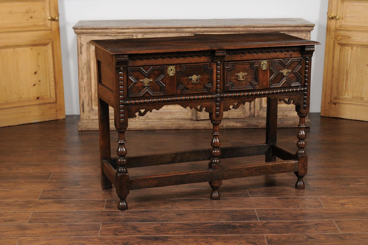 Server geometrico in quercia inglese della fine del XIX secolo, con due cassetti, grembiule intagliato, gambe tornite e barelle laterali. Nato in Inghilterra durante il terzo quarto del XIX secolo, questo squisito server in Oak presenta un piano