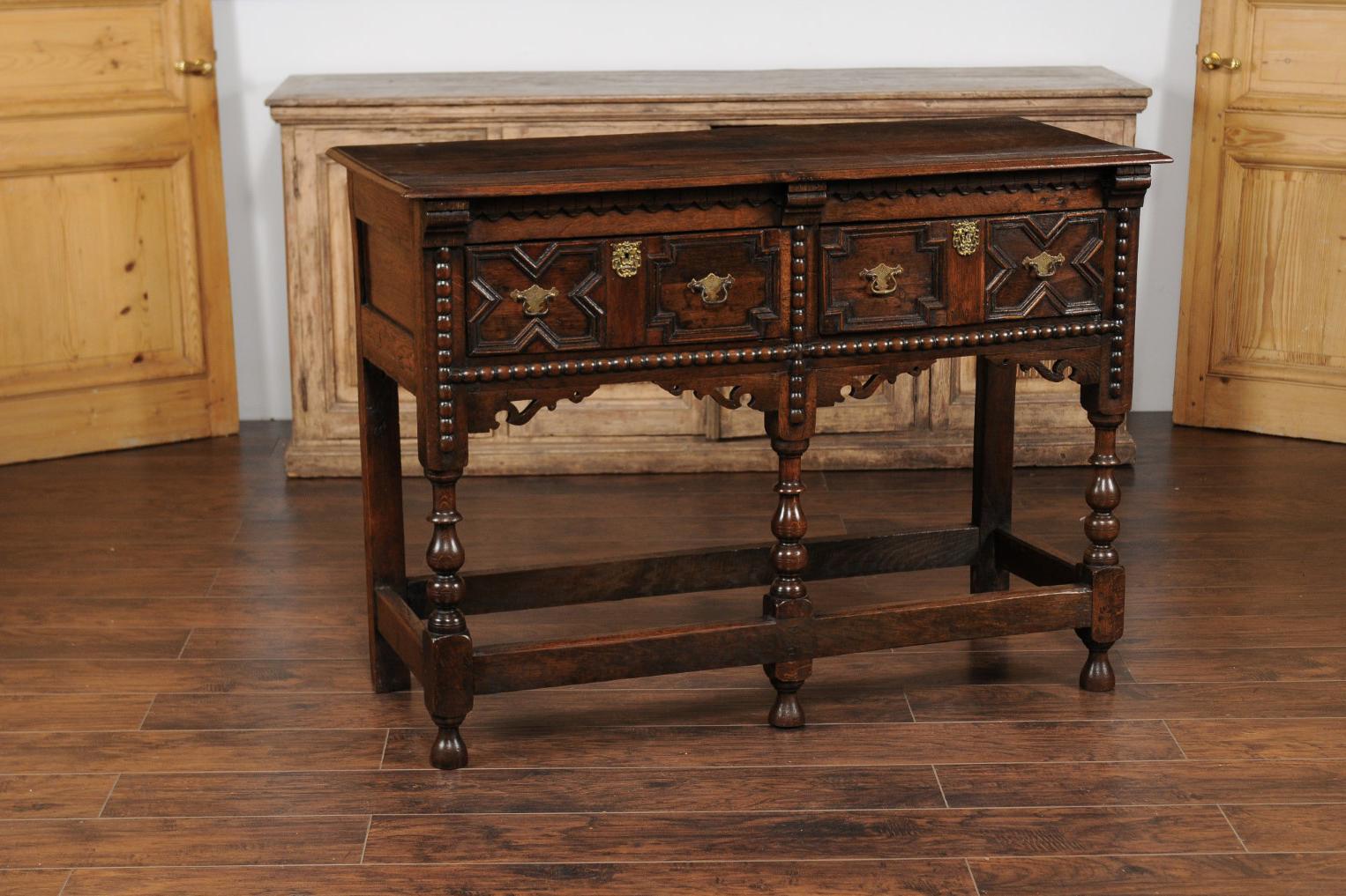 An English oak geometric front server from the late 19th century, with two drawers, carved apron, turned legs and side stretchers. Born in England during the third quarter of the 19th century, this exquisite oak server features a rectangular top