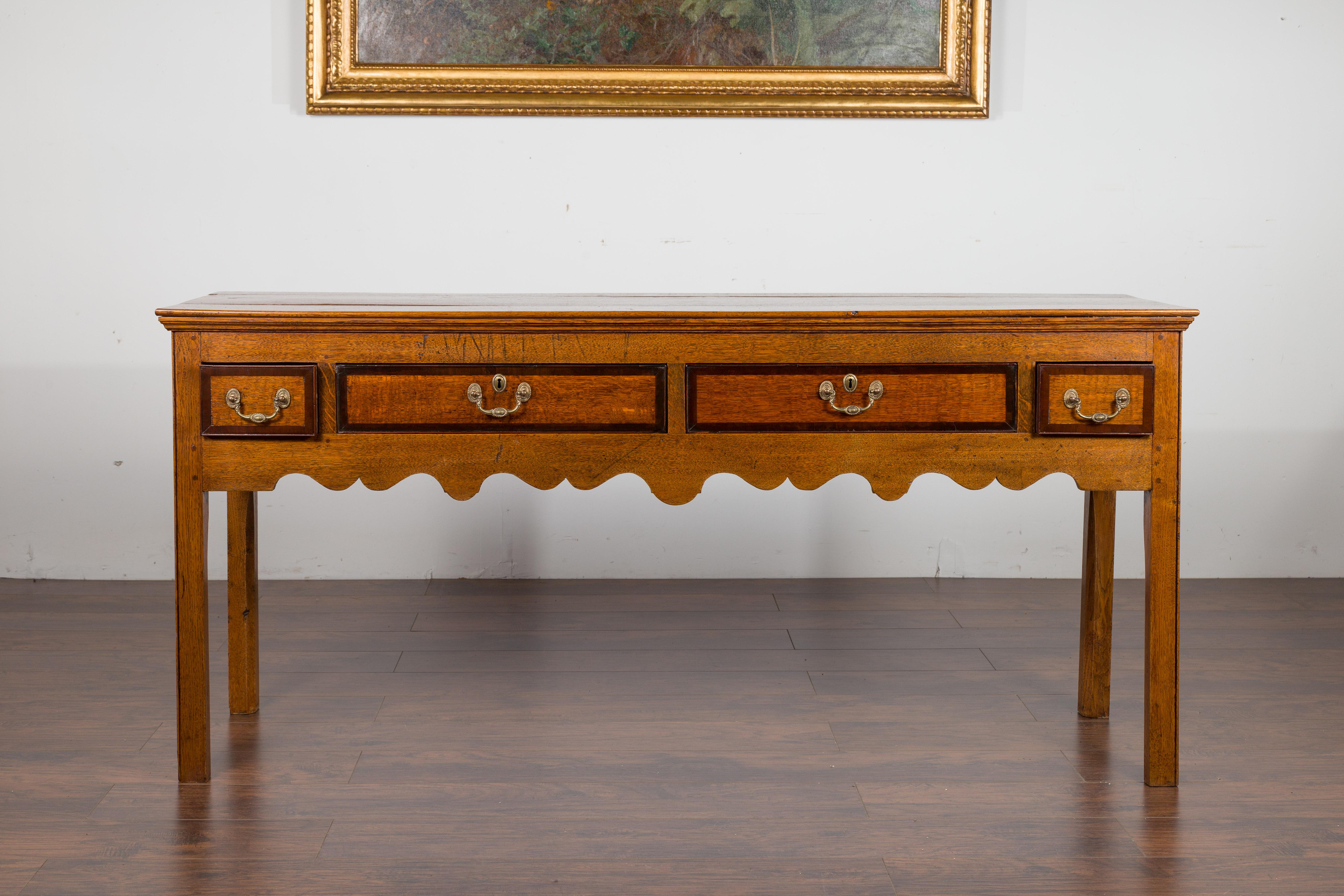 An English oak dresser base from the late 19th century, with four drawers and scalloped apron. Created in England during the third quarter of the 19th century, this oak dresser base features a rectangular planked top sitting above four two-toned