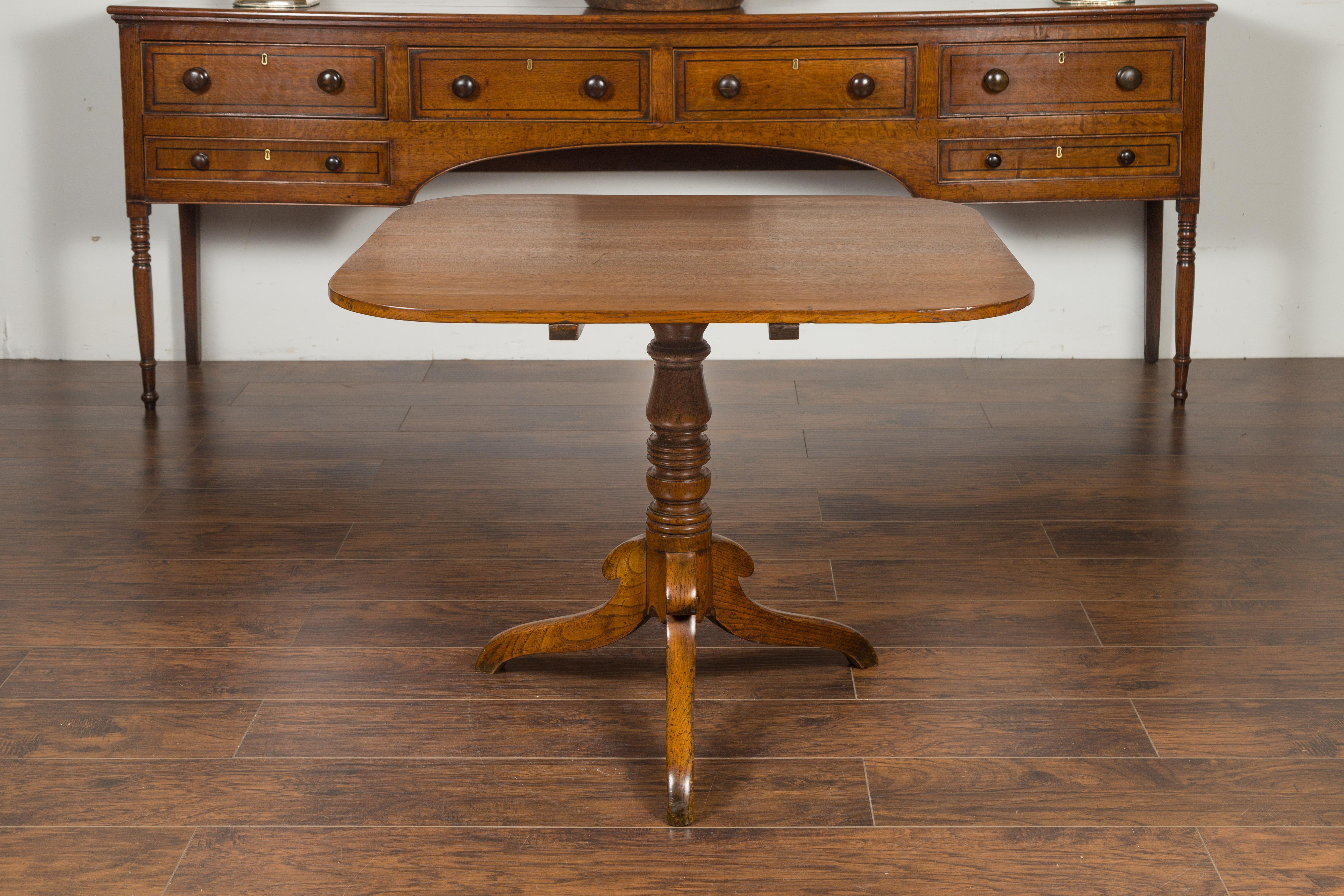An English oak tilt-top table from the late 19th century, with pedestal tripod base. Created in England during the third quarter of the 19th century, this oak table features a rectangular tilt-top with rounded corners, sitting above a turned
