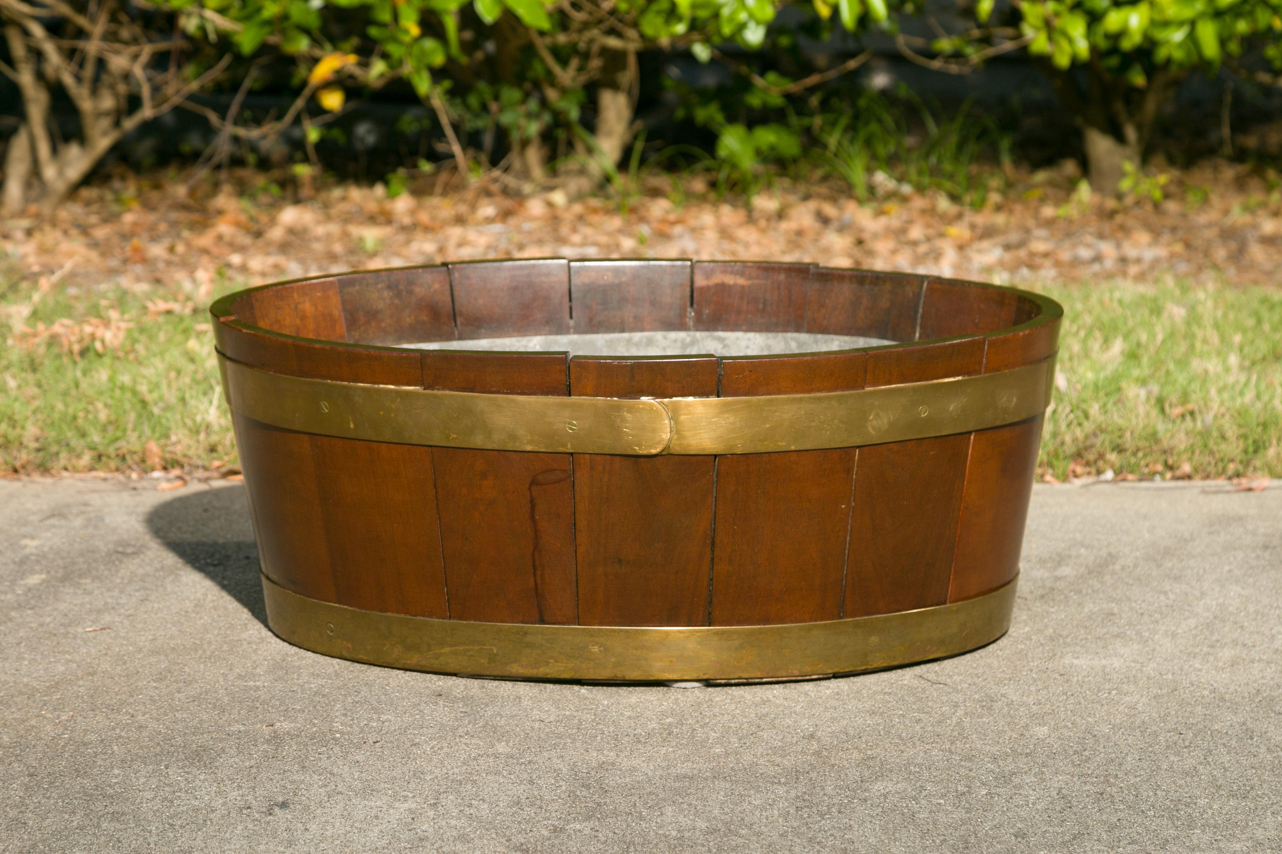 An English oval oak planter from the late 19th century with brass braces and liner. Used as a wine cooler or a planter, this oval piece, strengthened with horizontal brass braces whose golden hue compliments the brown color of the oak perfectly is