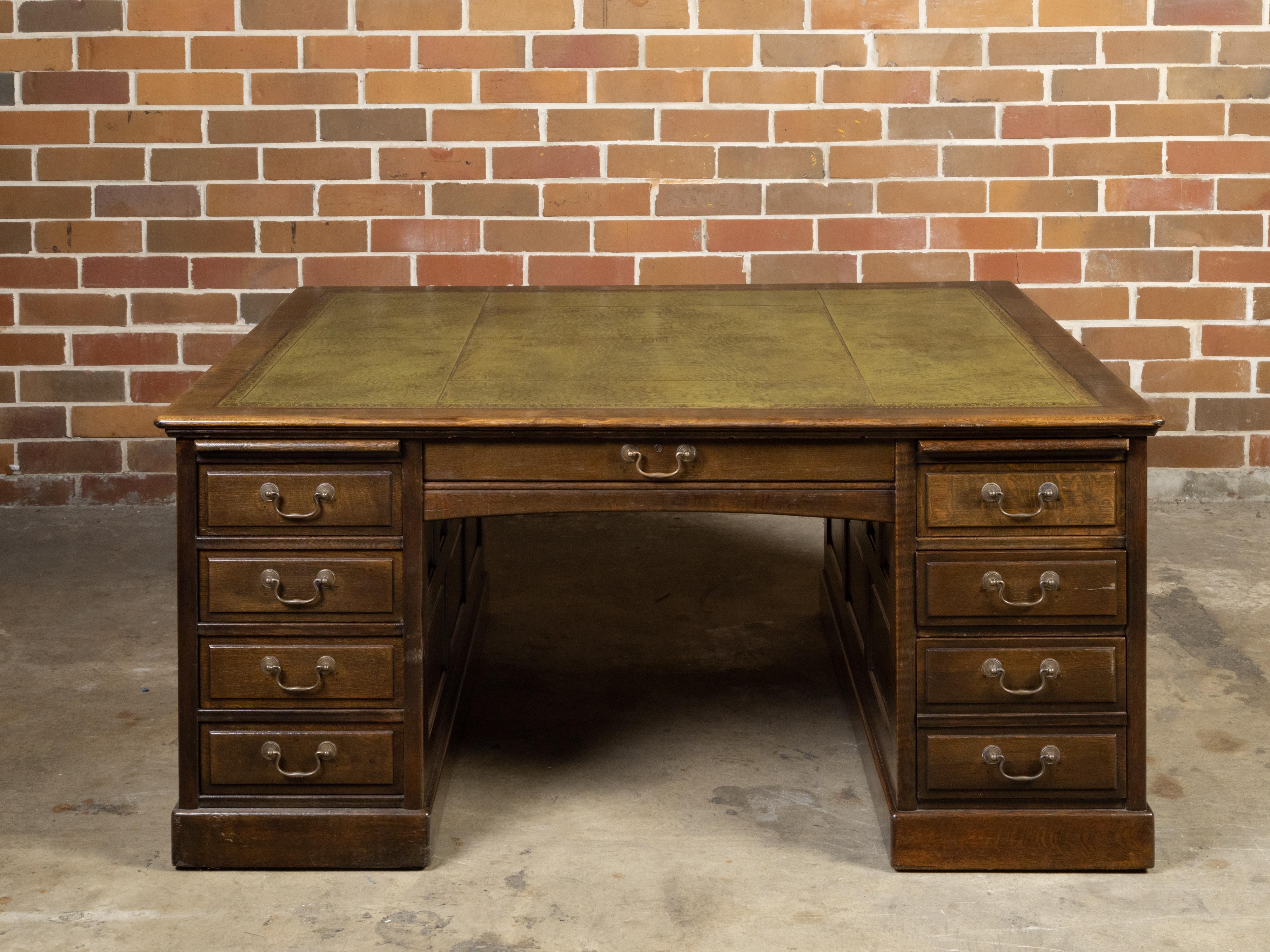An English oversized wooden partner's desk from the late 19th century, with green leather top, gilt scrolling accents, multiple drawers and pull-outs. Created in England during the third quarter of the 19th century, this partners' desk features a