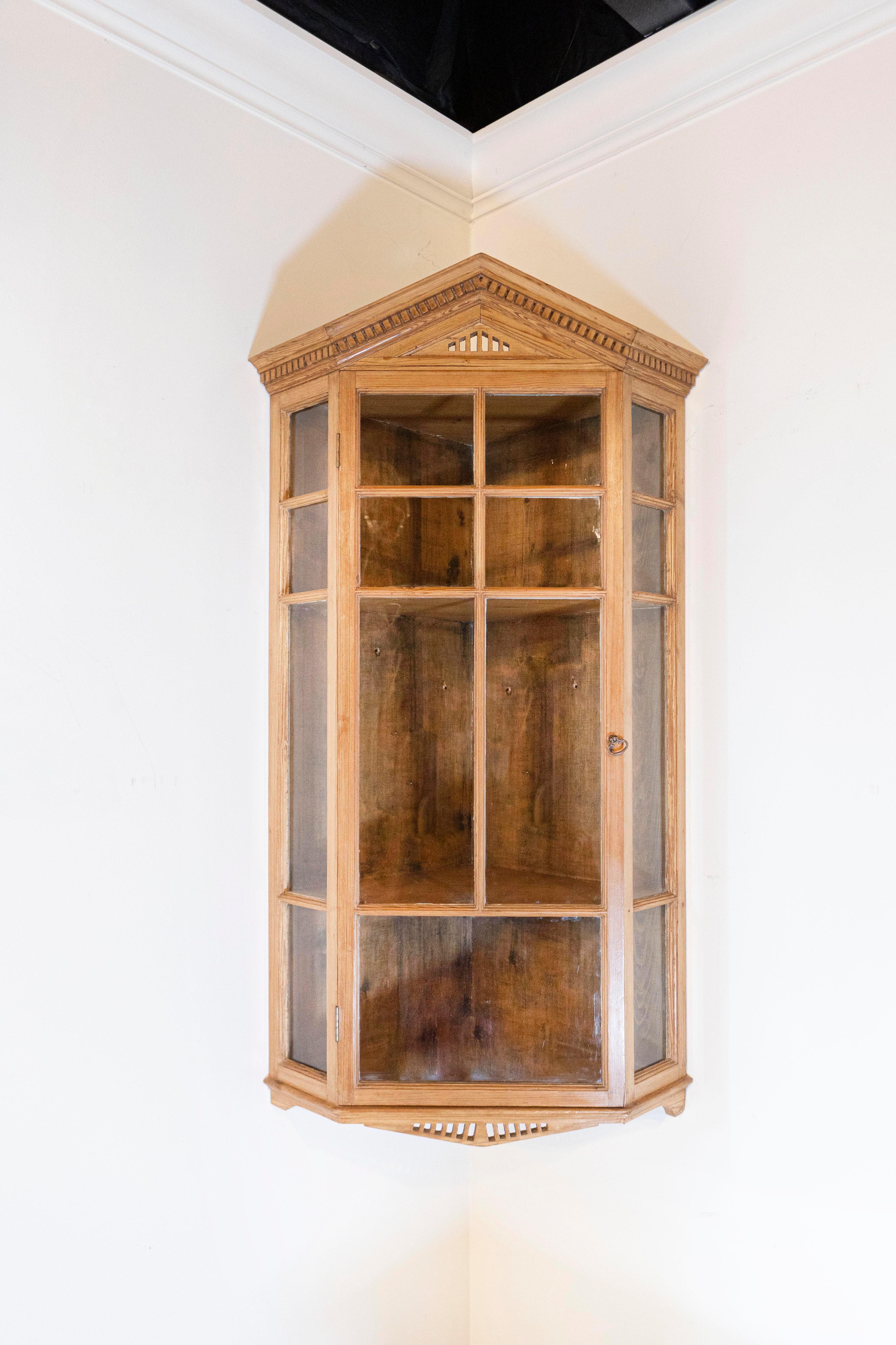 Armario esquinero colgante de pino inglés de finales del siglo XIX, con frontón puntiagudo, molduras dentiladas, puertas de cristal y esquinas inclinadas. Creado en Inglaterra durante el tercer cuarto del siglo XIX, este armario esquinero colgante