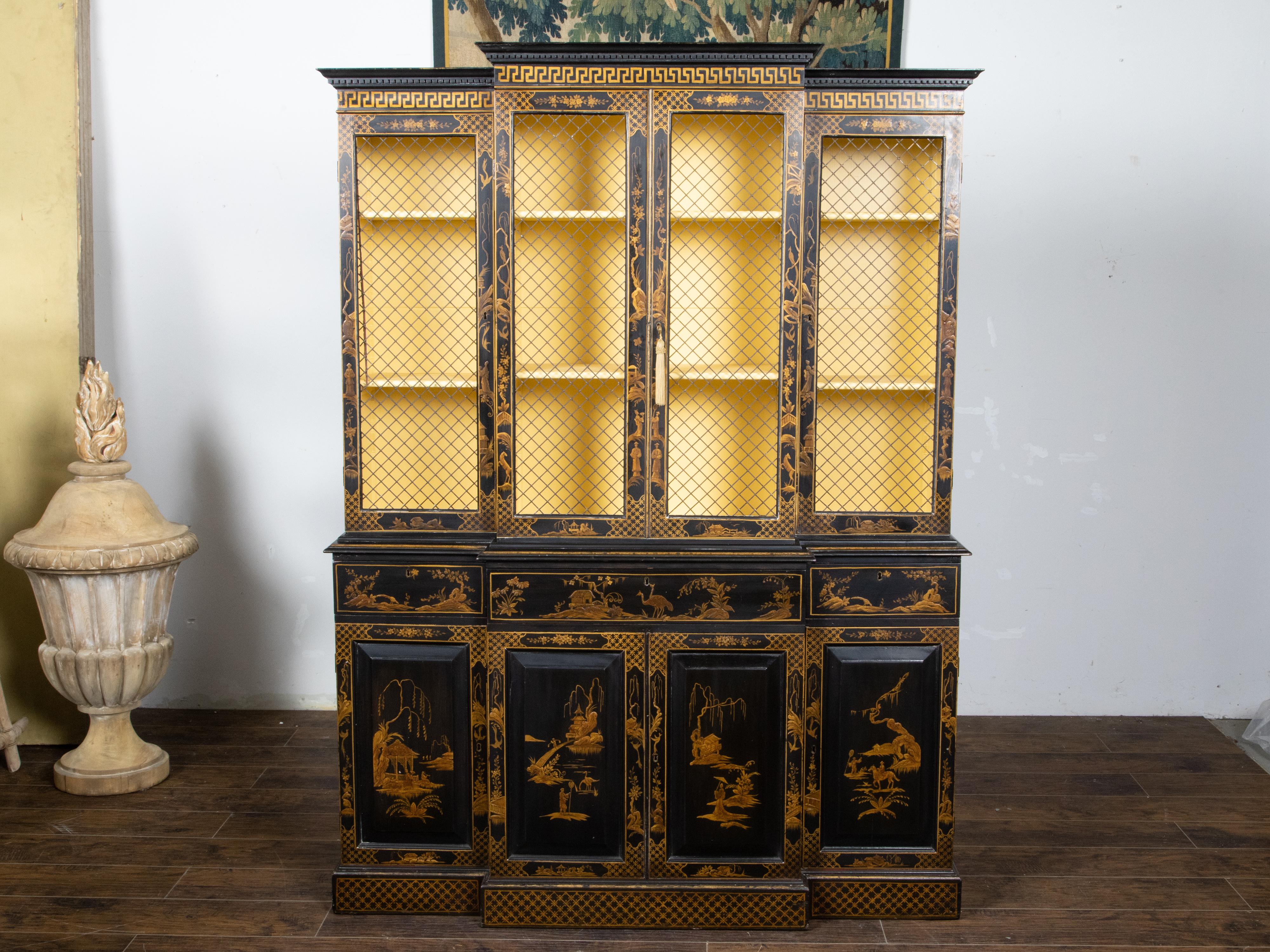 An English two part black and gold breakfront bookcase from the late 19th century with Chinoiserie décor, gilded Greek Key and floral décor, chicken wire doors, drawers and additional wooden doors. Created in England during the last quarter of the