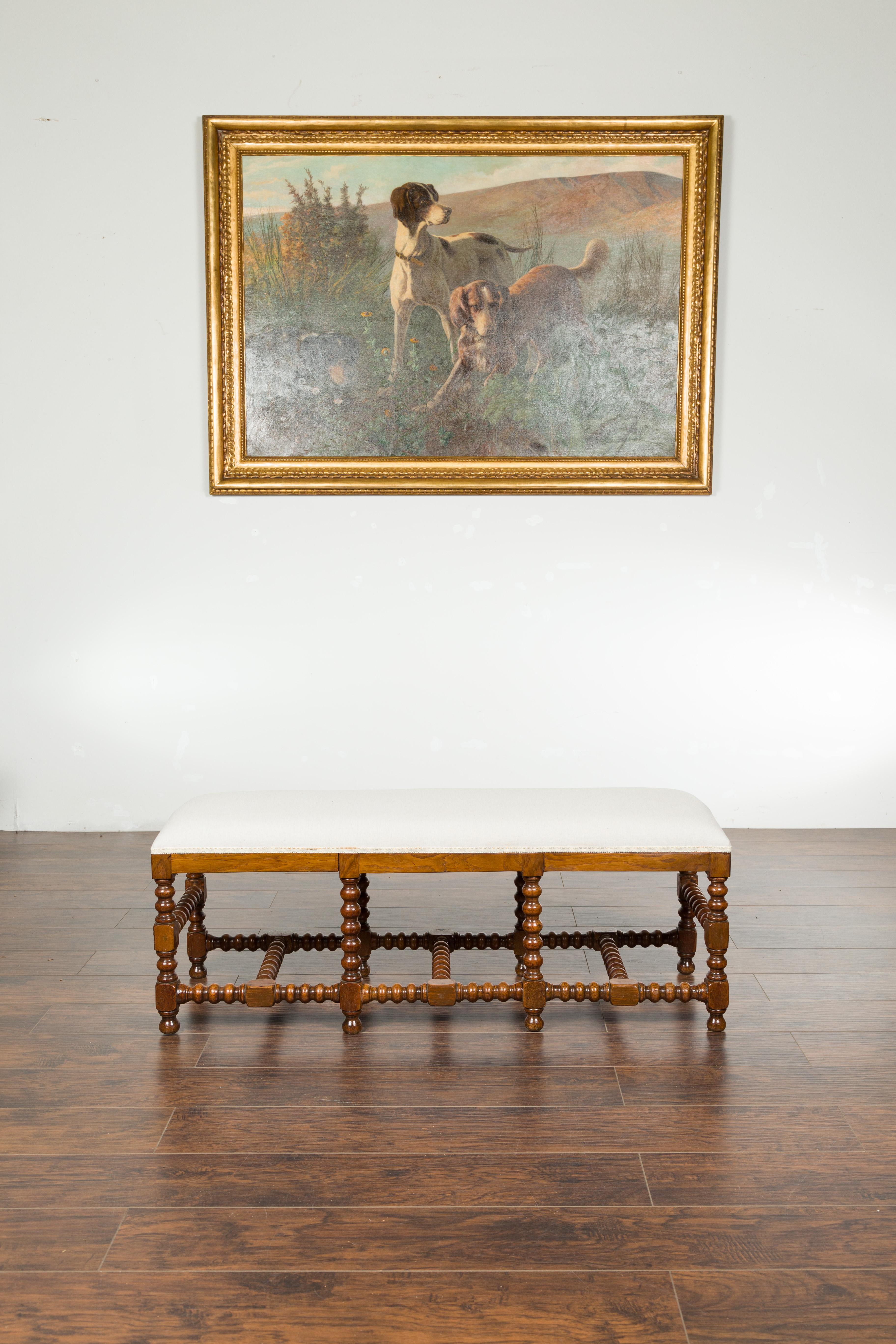 An English bobbin leg bench from the late 19th century, with new upholstery and cross stretchers. Created in England during the last quarter of the 19th century, this bench features a rectangular seat newly upholstered with a neutral toned fabric