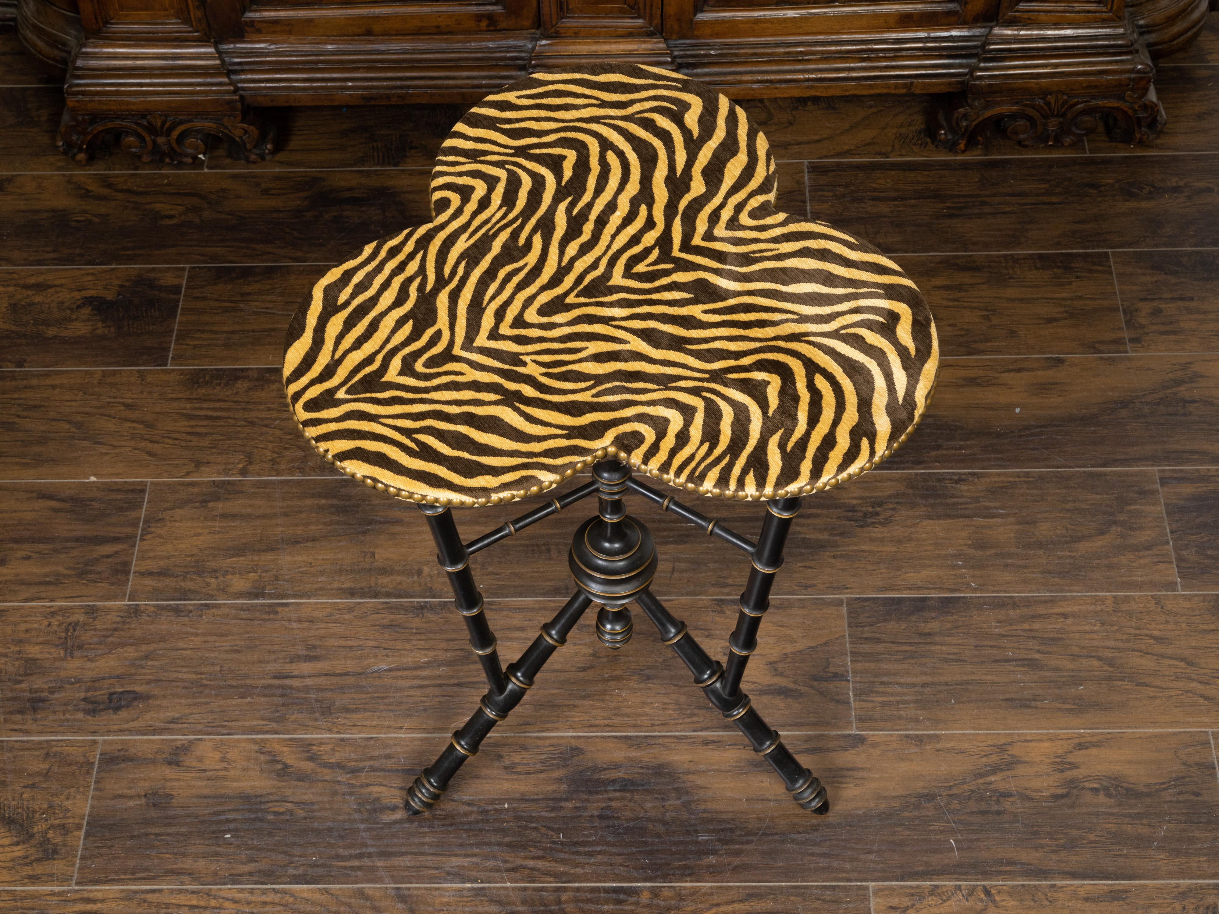 An English faux bamboo ebonized side table from the late 19th century, with clover leaf top and tiger upholstery. Created in England during the last quarter of the 19th century, this side table features a clover leaf top with faux tiger upholstery