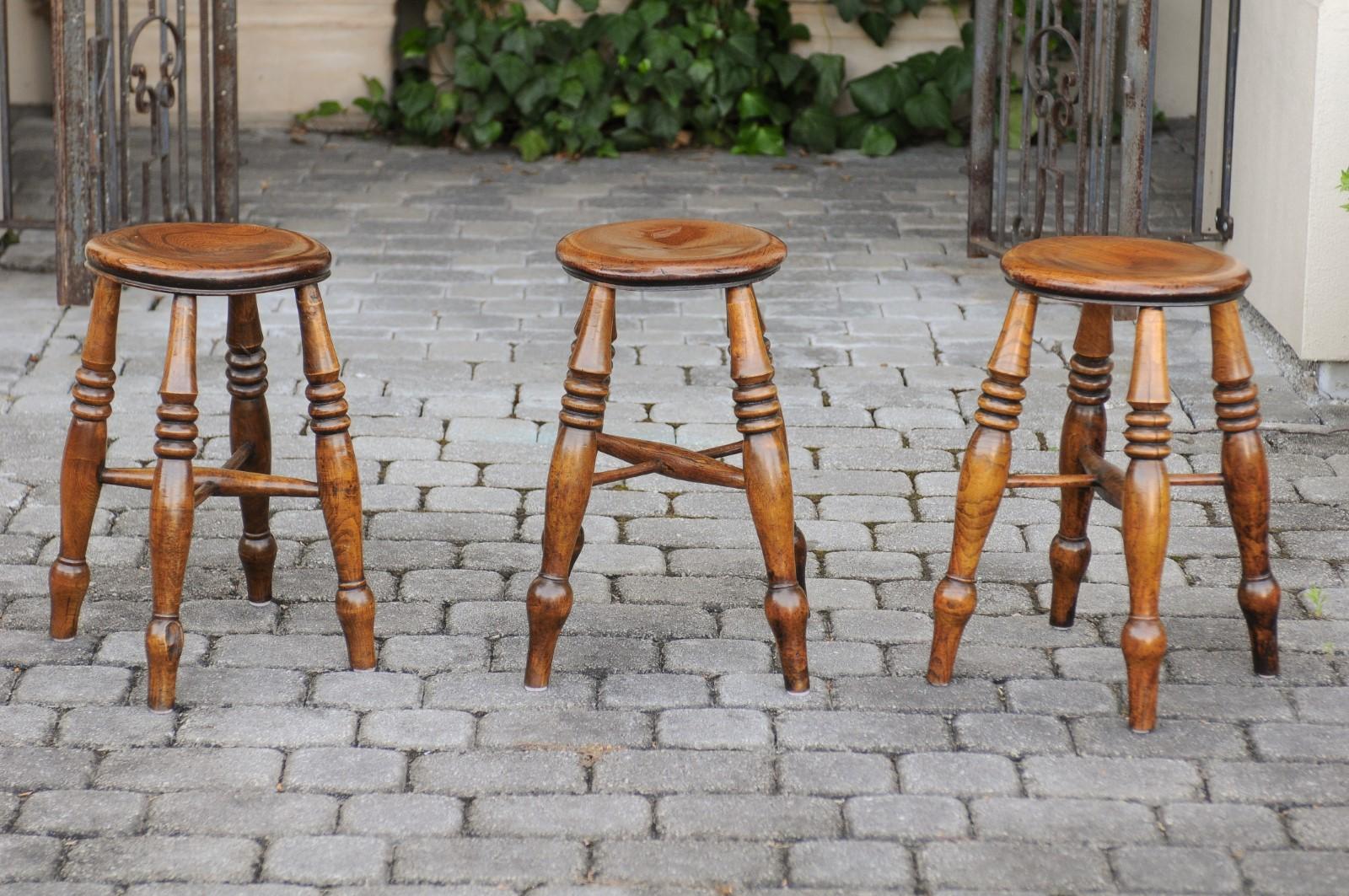 Three English elmwood stools from the late 19th century, with turned legs and cross stretchers. They are priced and sold individually. Born in England during the later years of the 19th century, each of these three elm stools features a circular top