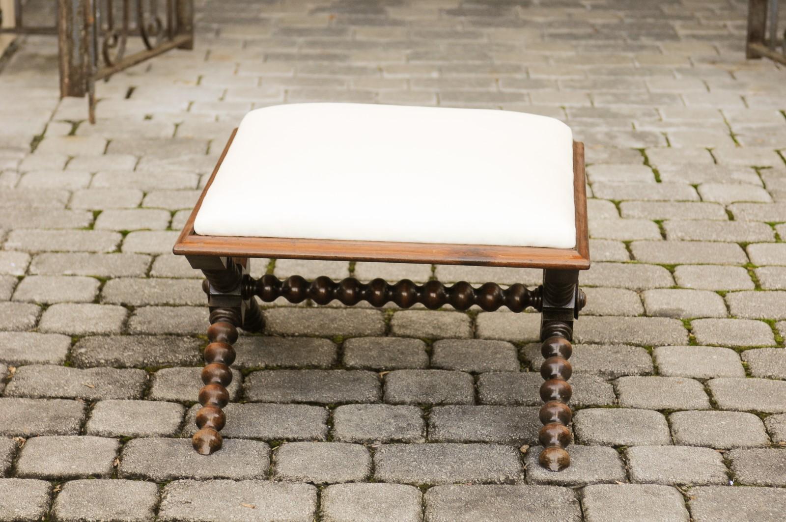 An English mahogany stool from the late 19th century, with spool legs and new upholstery. Born in England during the later years of the 19th century, this stylish mahogany stool features a rectangular seat, newly recovered with a simple muslin