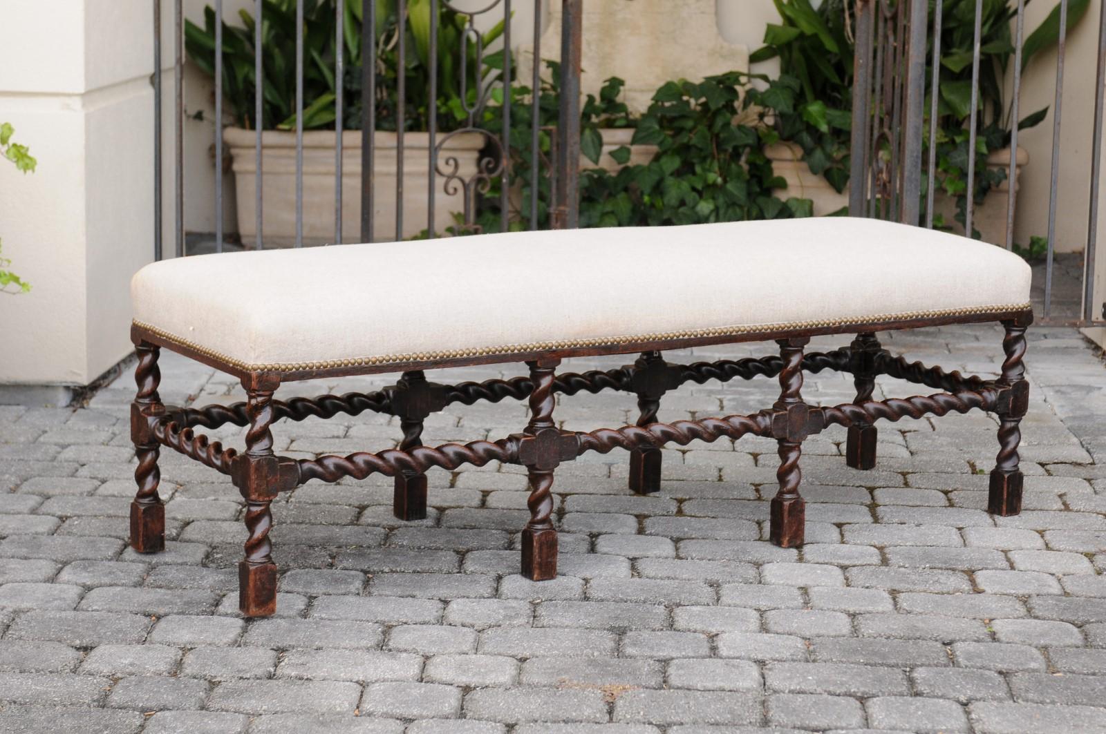 An English oak bench from the late 19th century, with barley twist base, dark patina and new upholstery. Born in England during the last quarter of the 19th century, this exquisite oak bench features a long rectangular seat covered with a linen
