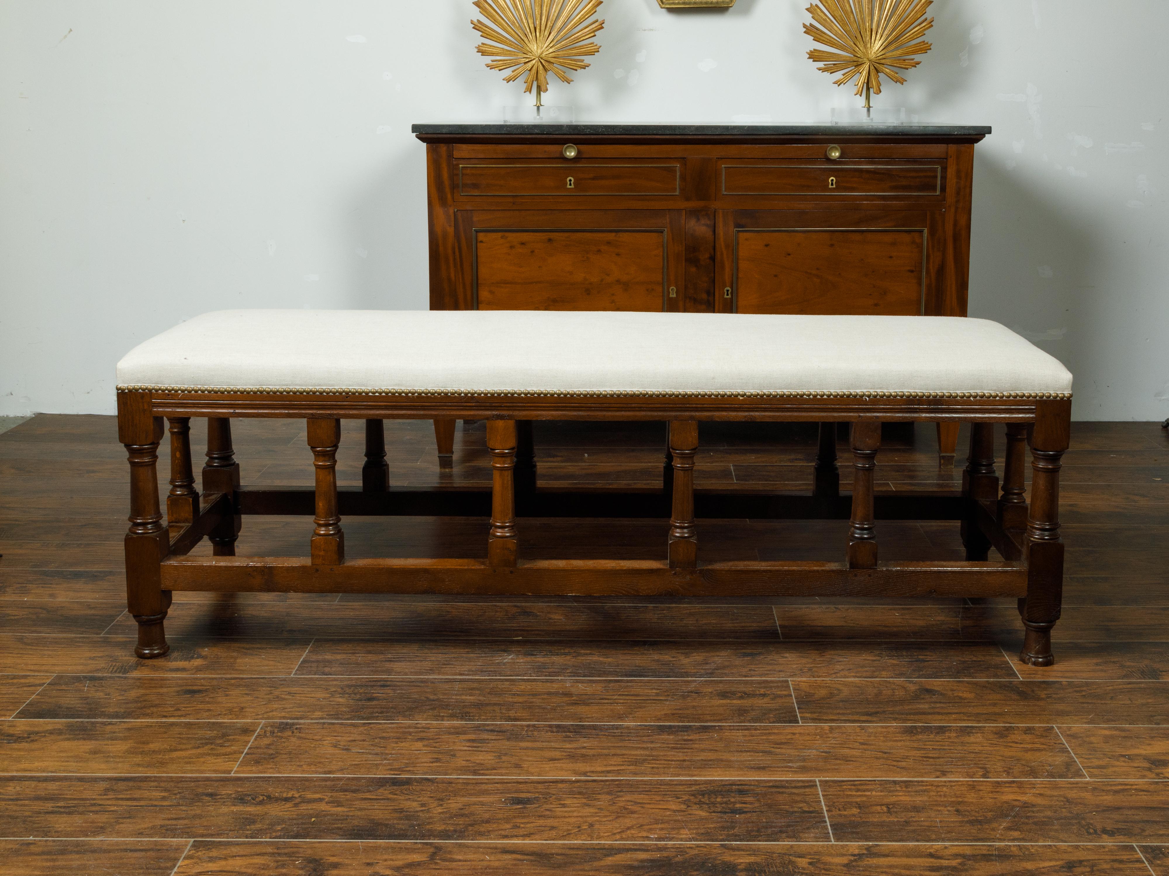 An English oak bench from the late 19th century, with turned legs and new upholstery. Created in England during the last quarter of the 19th century, this oak bench features a long rectangular seat newly recovered with a neutral toned fabric secured