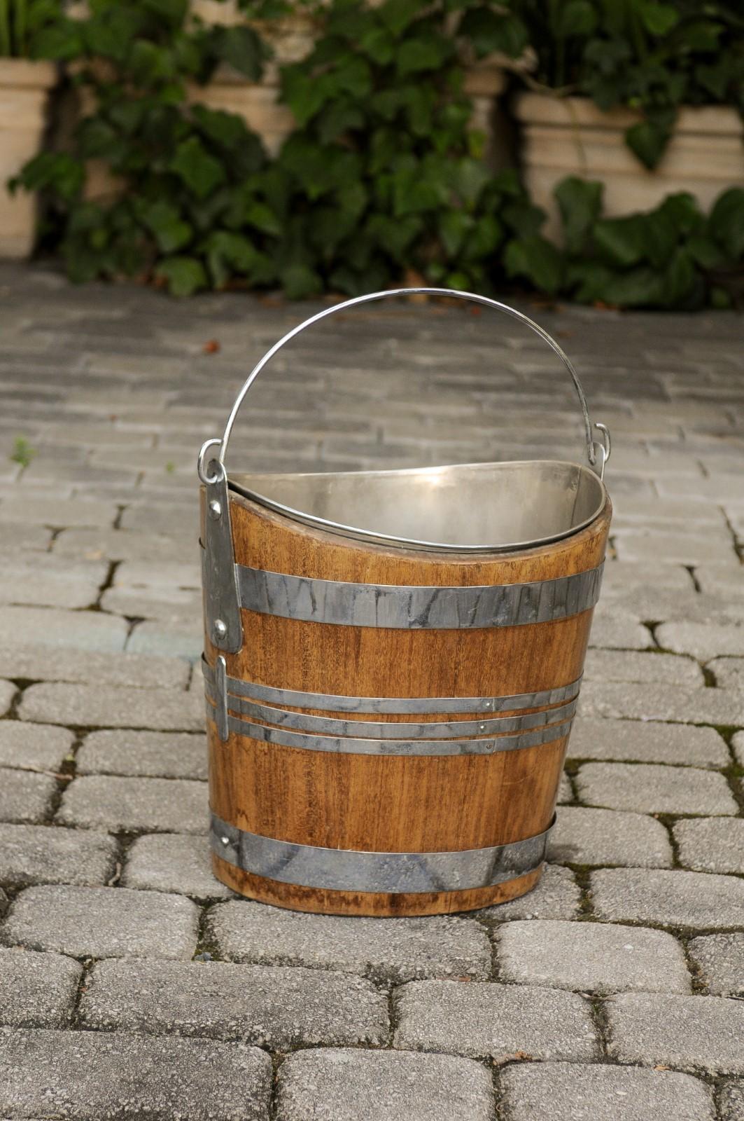 An English oak bucket from the late 19th century, with silver plated of steel accents, liner and large handle. Born in England during the later years of the 19th century, this oak bucket features an unusual silver plated or steel horizontal