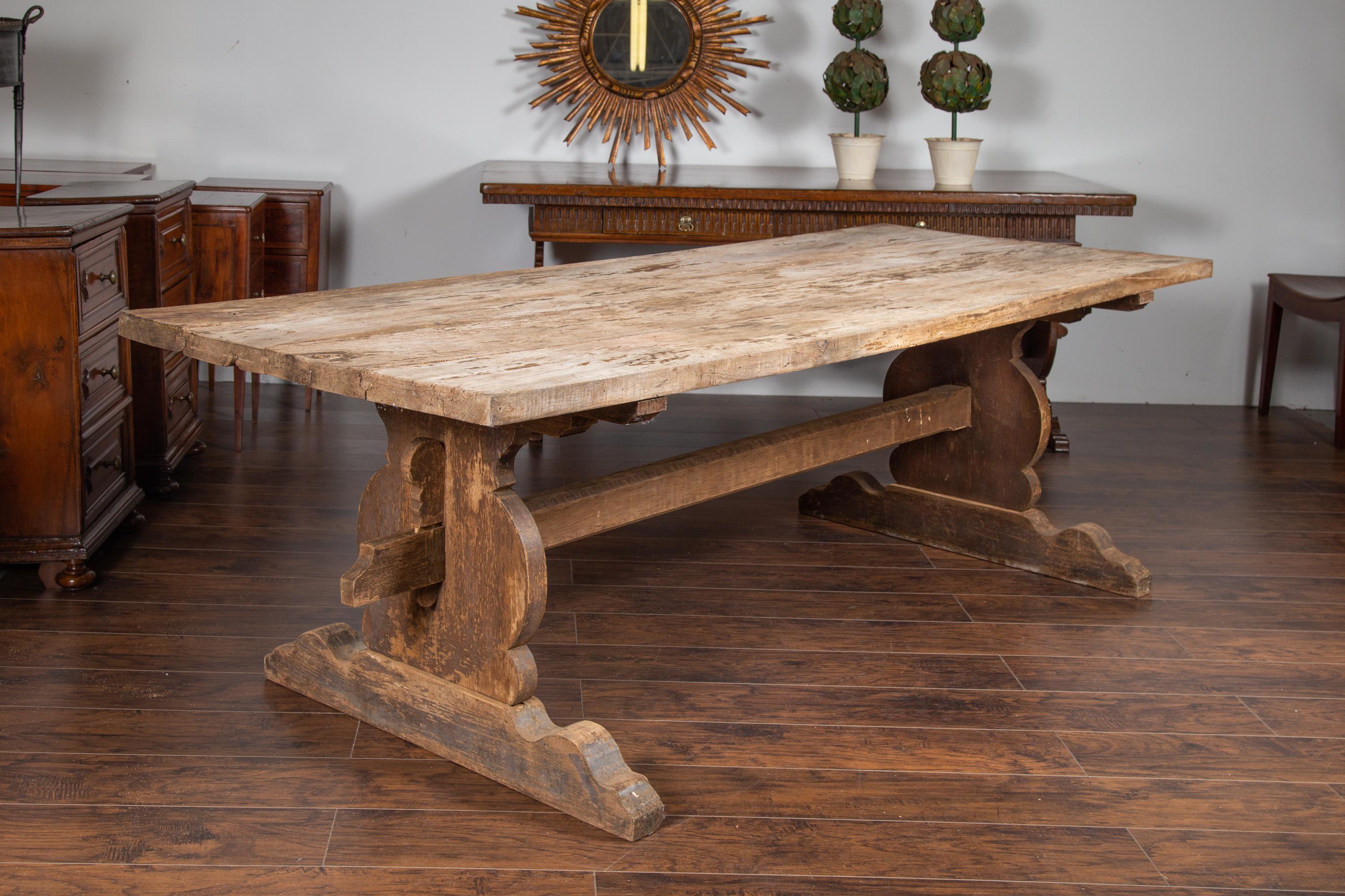 An English oak farm table from the late 19th century, with carved trestle base and weathered appearance. Born in England during the last quarter of the 19th century, this exquisite farm table features a rectangular removable planked top presenting a