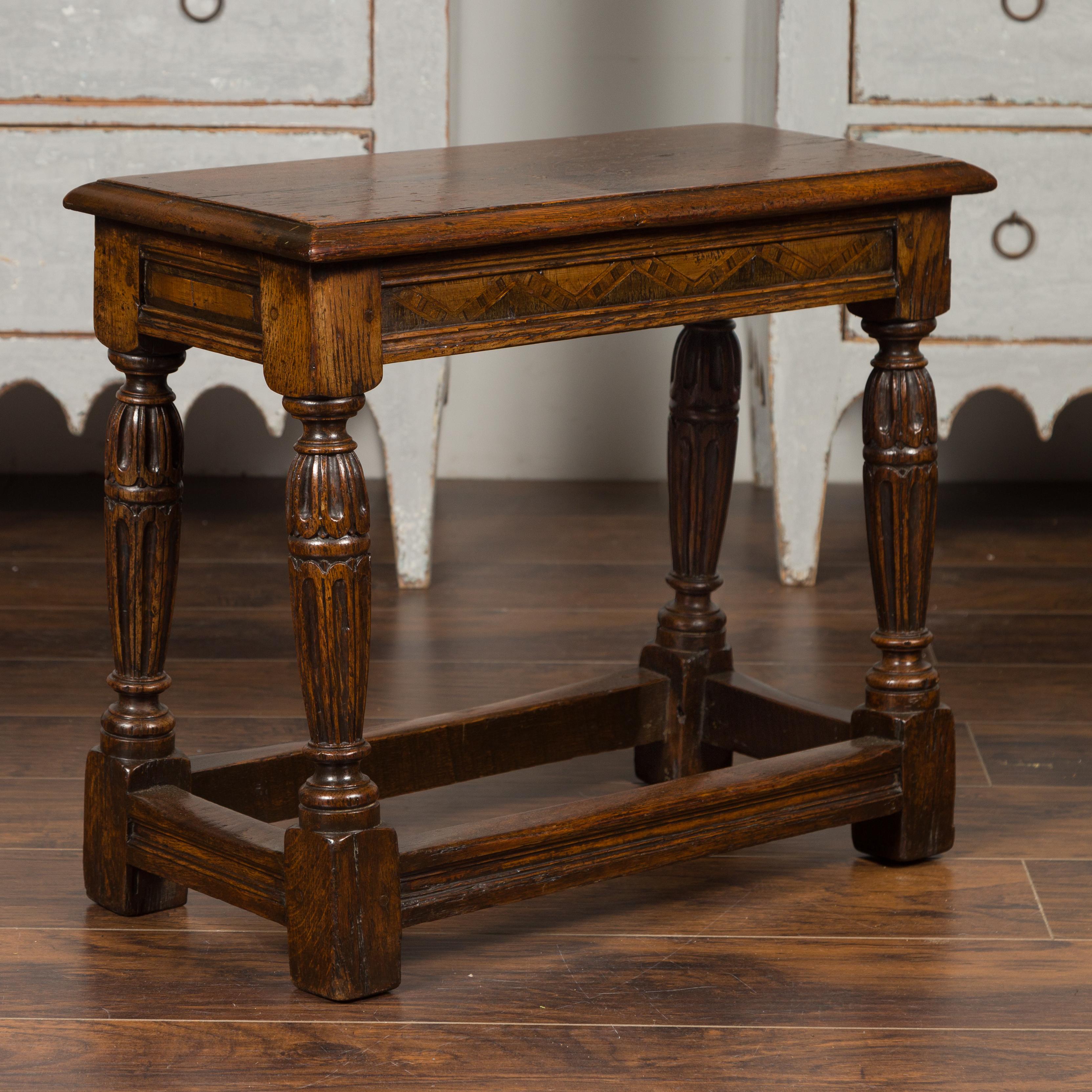 An English oak joint stool from the late 19th century, with carved turned legs, inlaid apron and side stretchers. Born in England during the last quarter of the 19th century, this exceptional joint stool features a rectangular seat with beveled