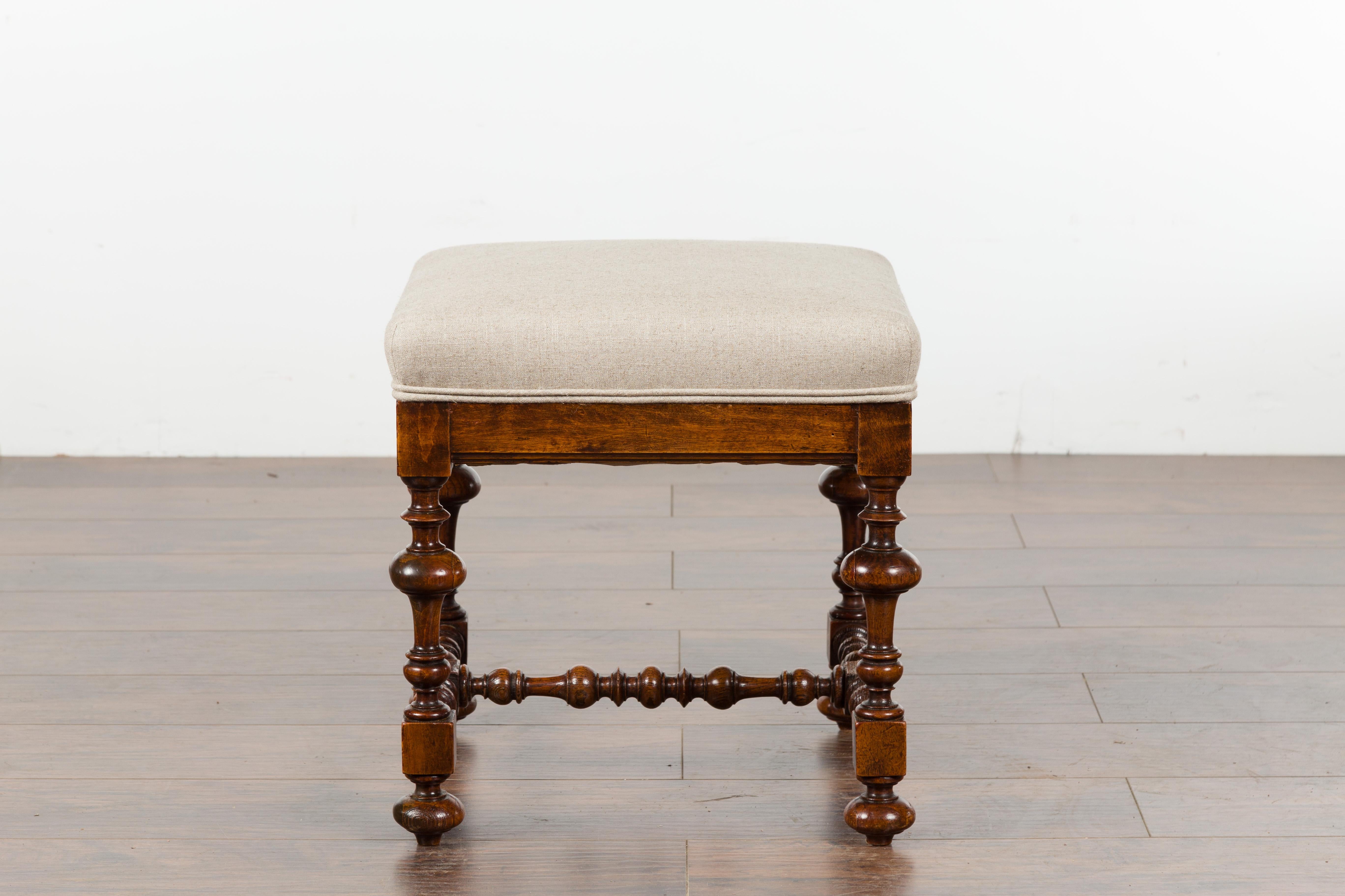 A small English oak stool from the late 19th century, with turned base and new upholstery. Created in England during the last quarter of the 19th century, this oak stool features a square top newly recovered with a linen, double welt fabric. The