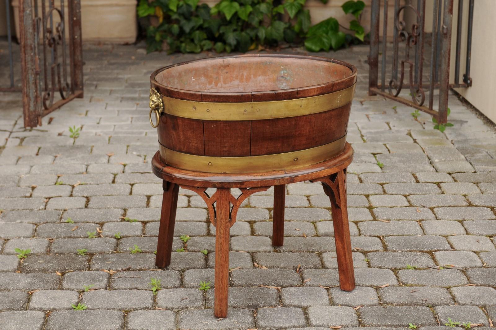 An English oval oak planter from the late 19th century, with brass braces, lion rings pulls and newer custom oak stand. Born in England during the later years of the 19th century, this charming oval planter is made of oak slats secured behind