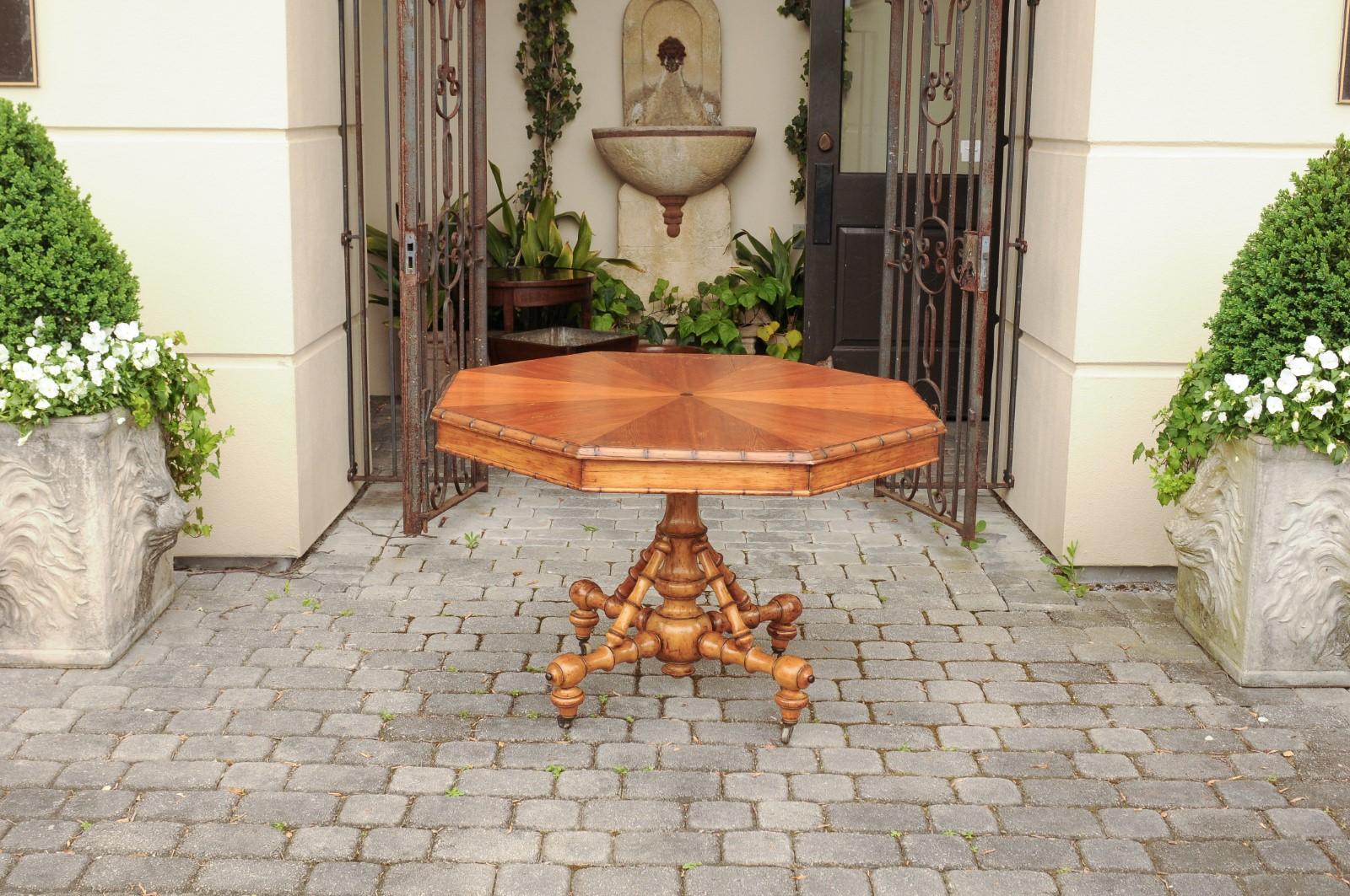 An English pine octagonal table from the late 19th century, with radiating veneer and intricate faux-bamboo base on casters. Born in England during the later years of the 19th century, this charming table features an unusual octagonal top with