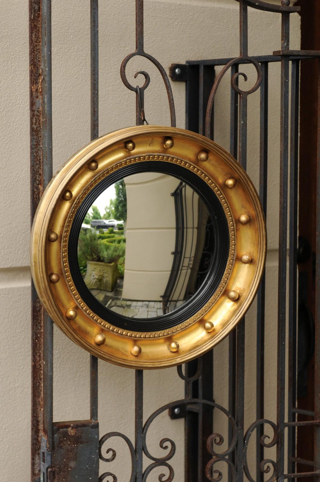 A small English giltwood bull’s-eye convex girandole mirror from the late 19th century with ebonized accents and petite spheres. Born in the later years of the 19th century, this stylish English circular mirror features a convex mirror plate,