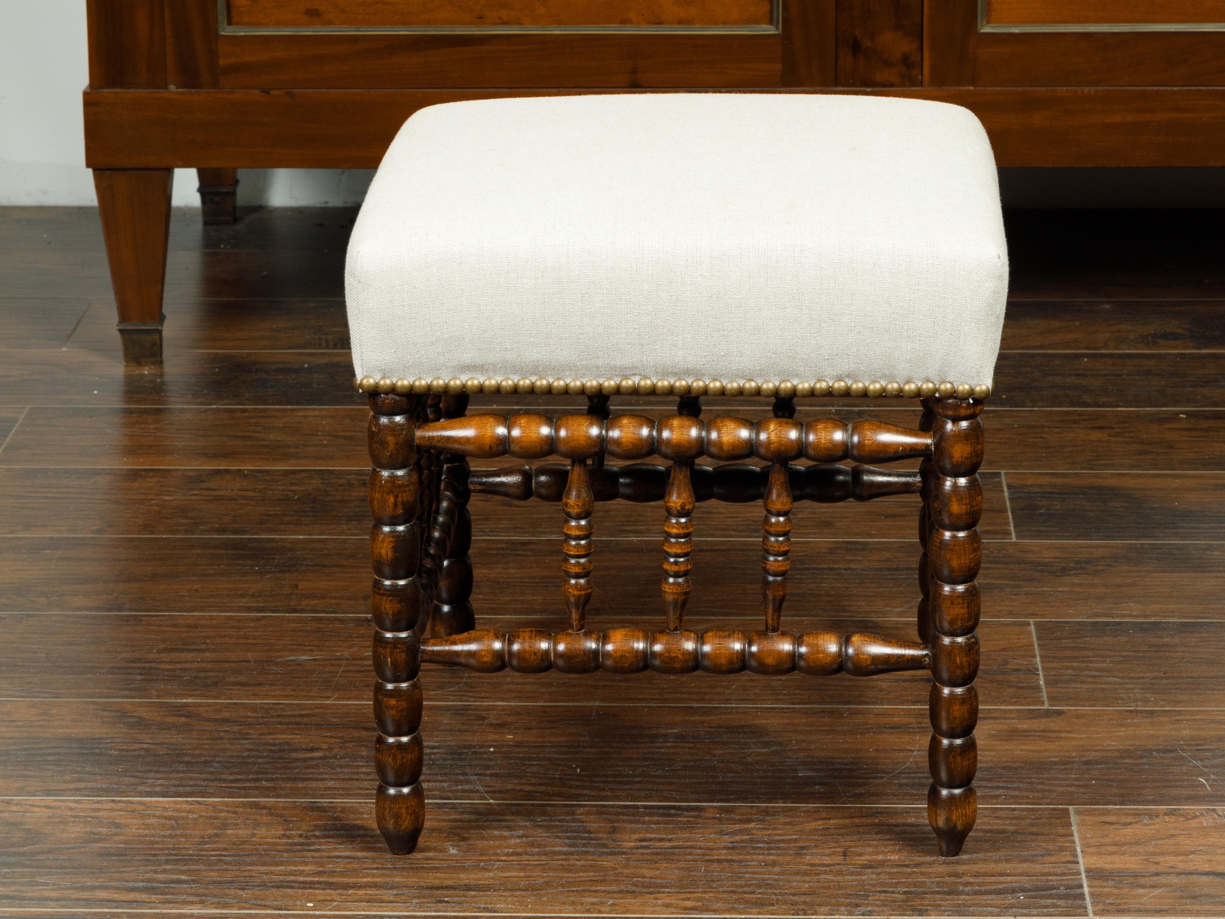 An English bobbin stool from the late 19th century, with new upholstery and side stretchers. Created in England during the last quarter of the 19th century, this stool features a square top newly reupholstered with a neutral toned fabric secured