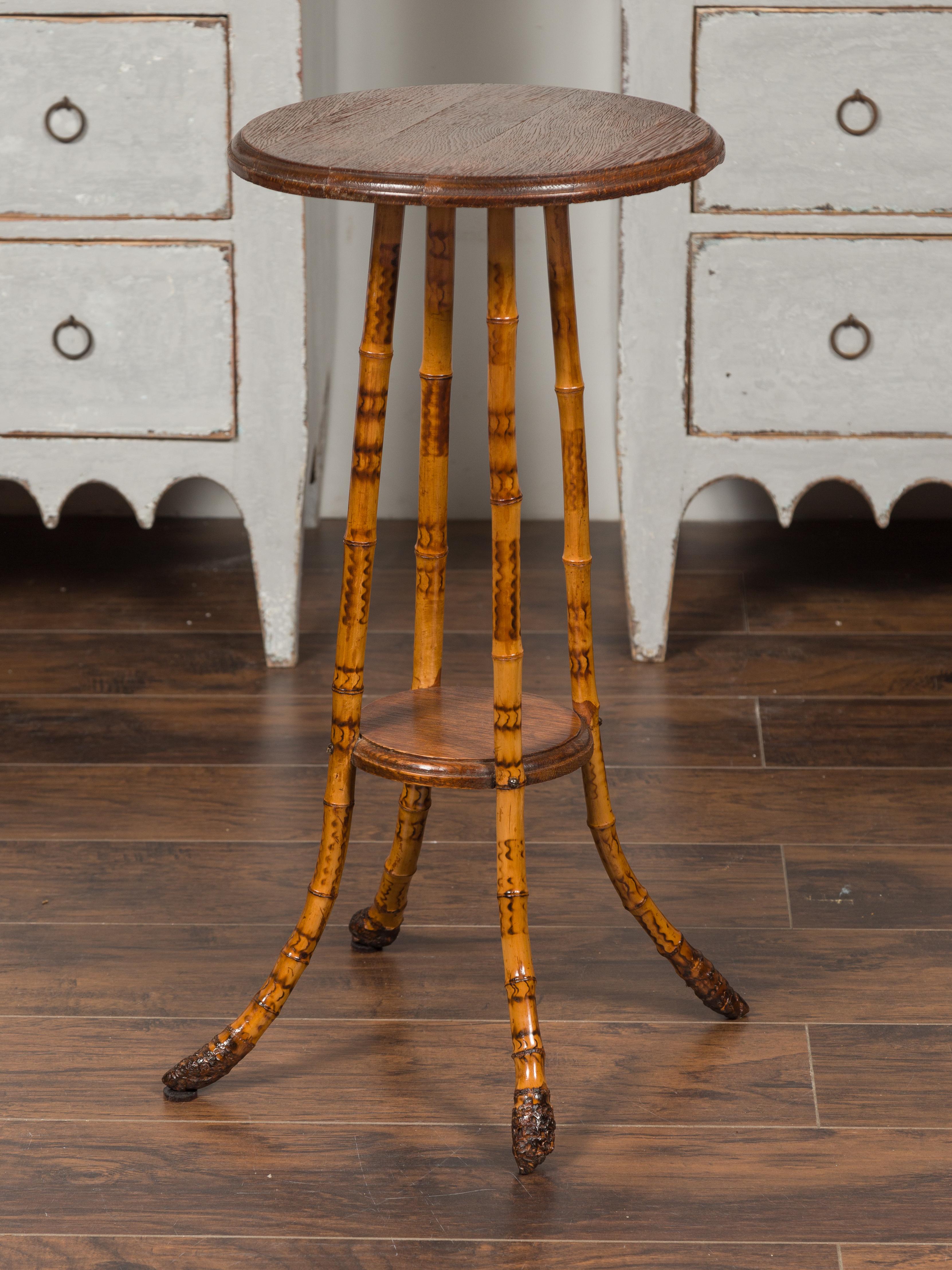 An English bamboo side table from the late 19th century, with circular top and small lower shelf. Born in England during the late decade of the 19th century, this side table features a round wooden top, sitting above four bamboo splaying legs