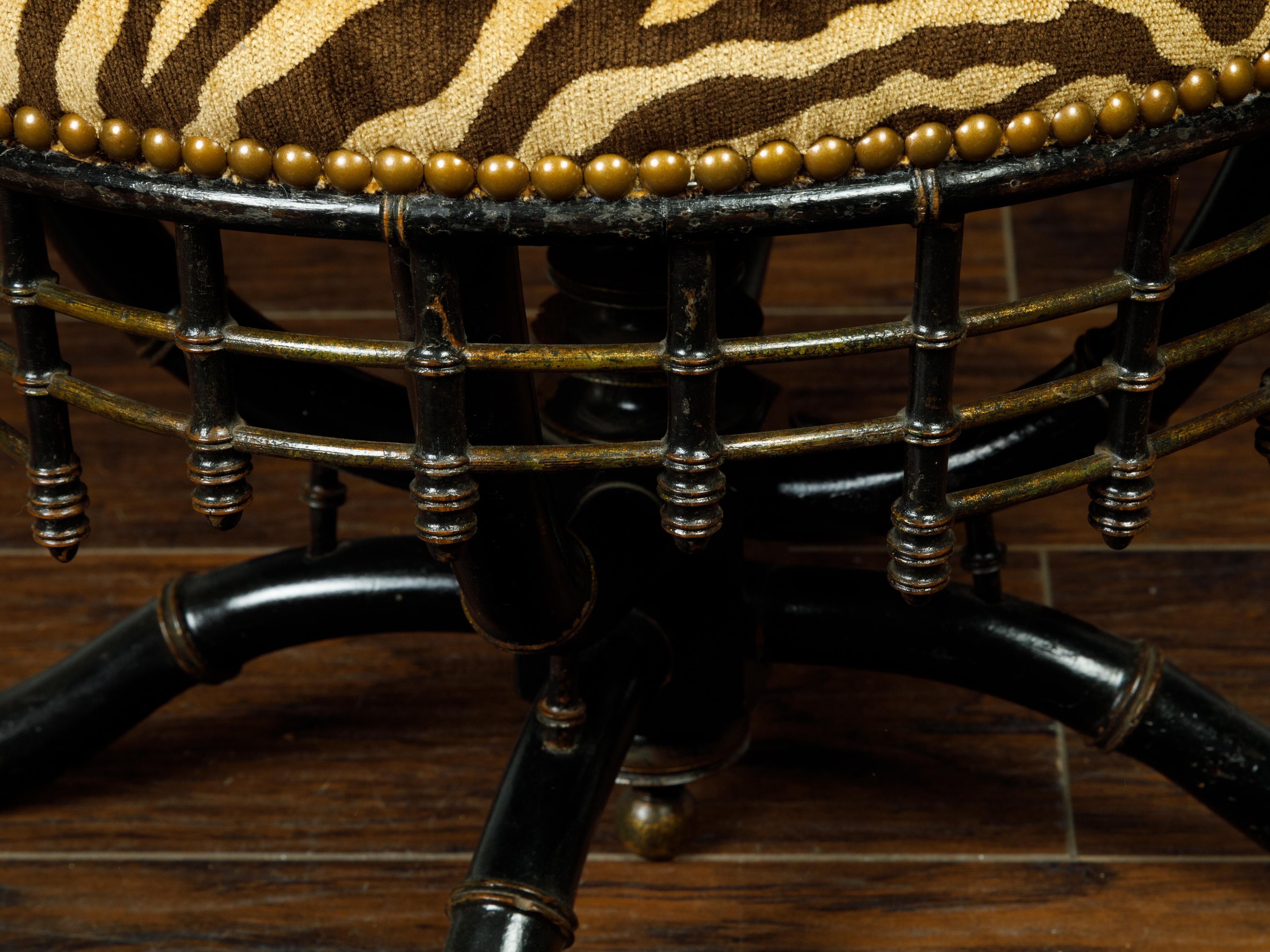 An English ebonized faux bamboo stool from the late 19th century, with tiger upholstery. Created in England during the last decade of the 19th century, this stool features a circular seat recovered with a tiger striped upholstery. The stool is