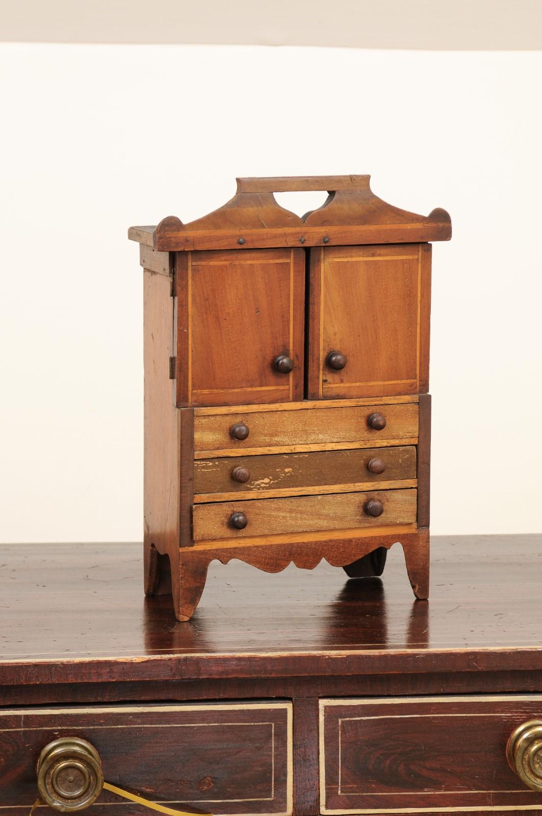 An English fruitwood miniature cabinet from the late 19th century, with two petite doors and three drawers. Created in England during the last quarter of the 19th century, this fruitwood cabinet charms us with its very small proportions and rustic