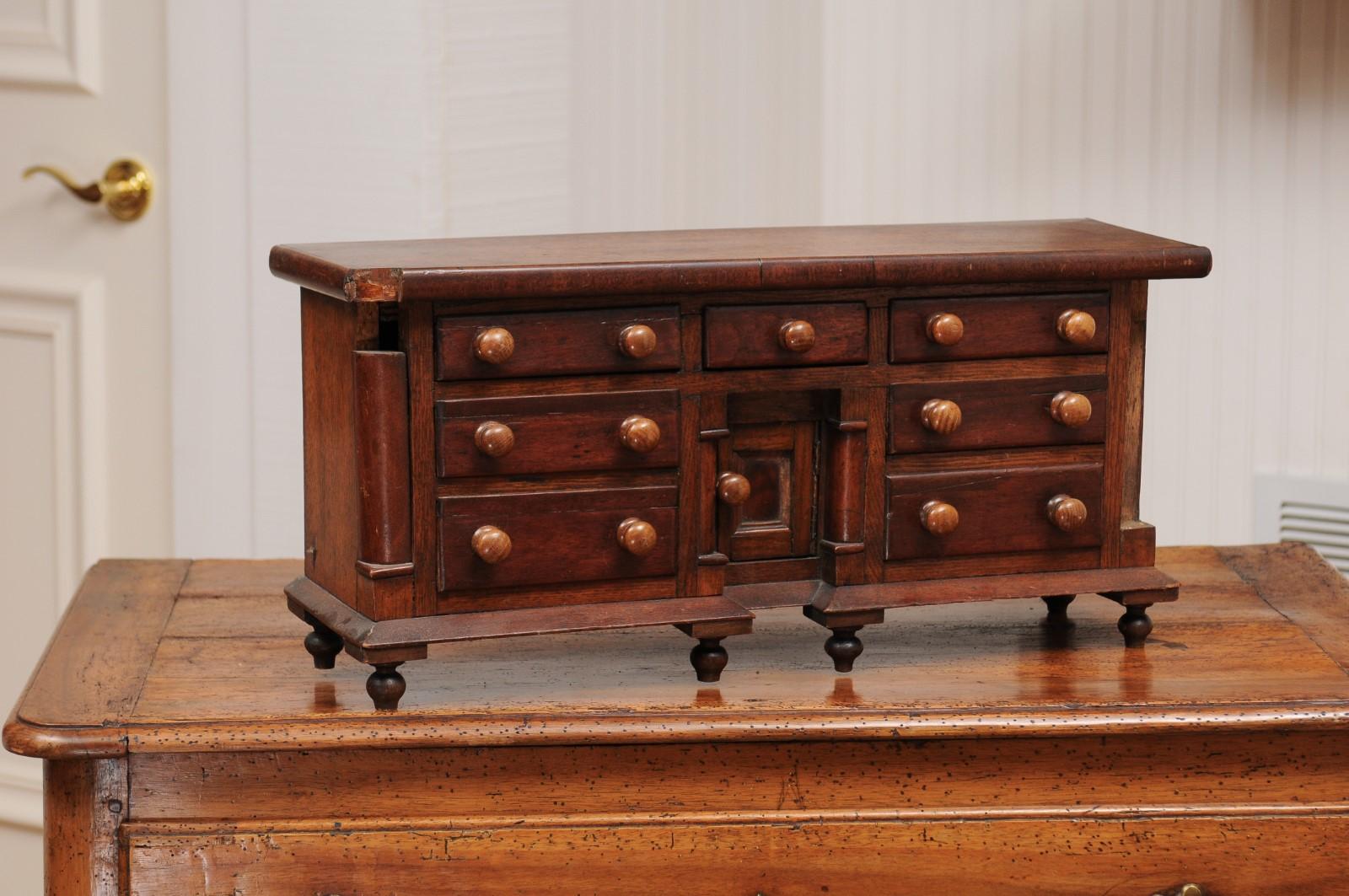 An English miniature chest from the late 19th century, with seven drawers, semi columns and turnip feet. Created in England during the last decade of the 19th century, this miniature piece, likely a salesman sample due to its petite proportions,