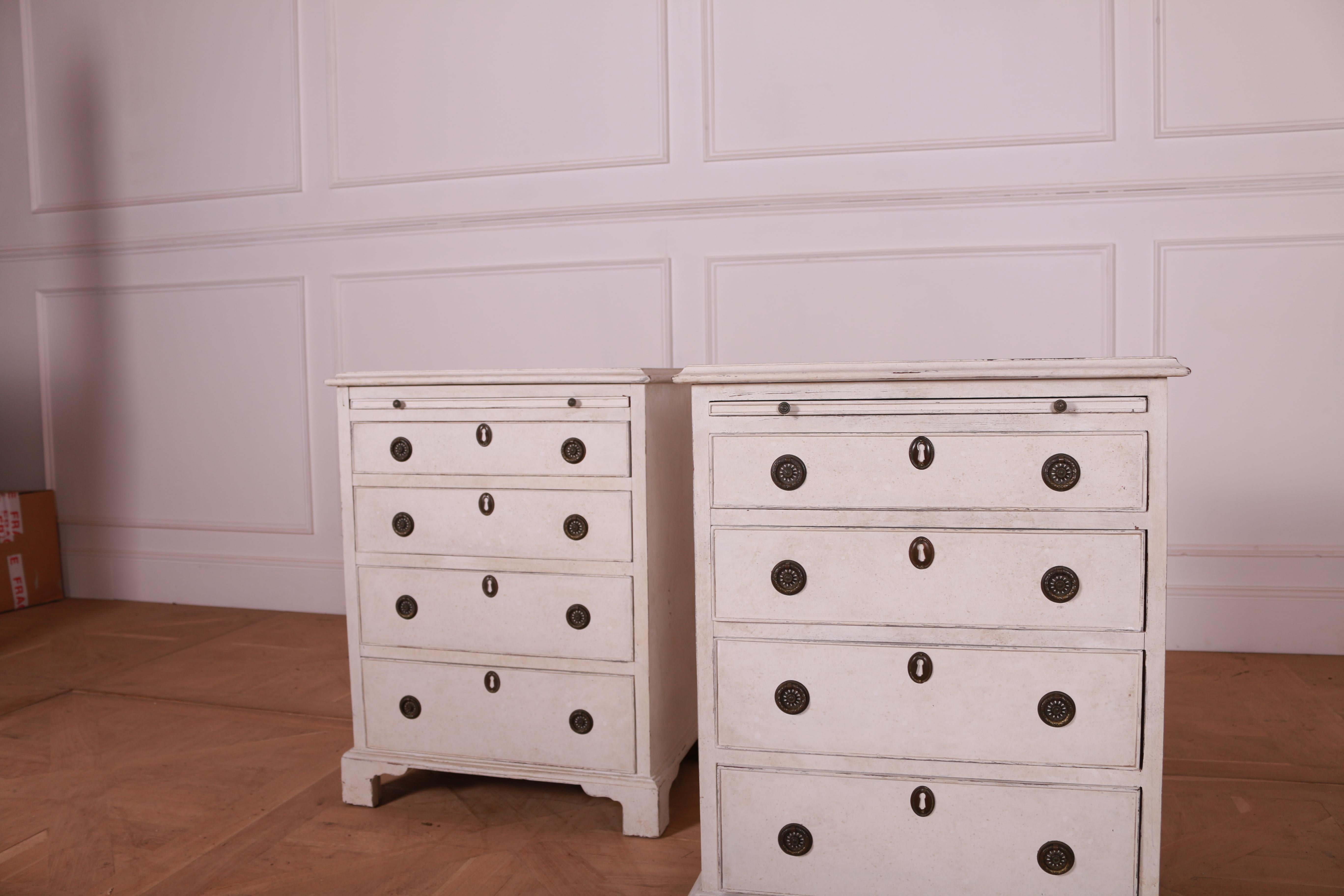 A pair of English pine commodes from circa 1890 with antique off white painted finish, pull-out drawer followed by four graduating ones, and carved bracket feet. Envision these quintessentially English pine commodes from circa 1890 as a charming